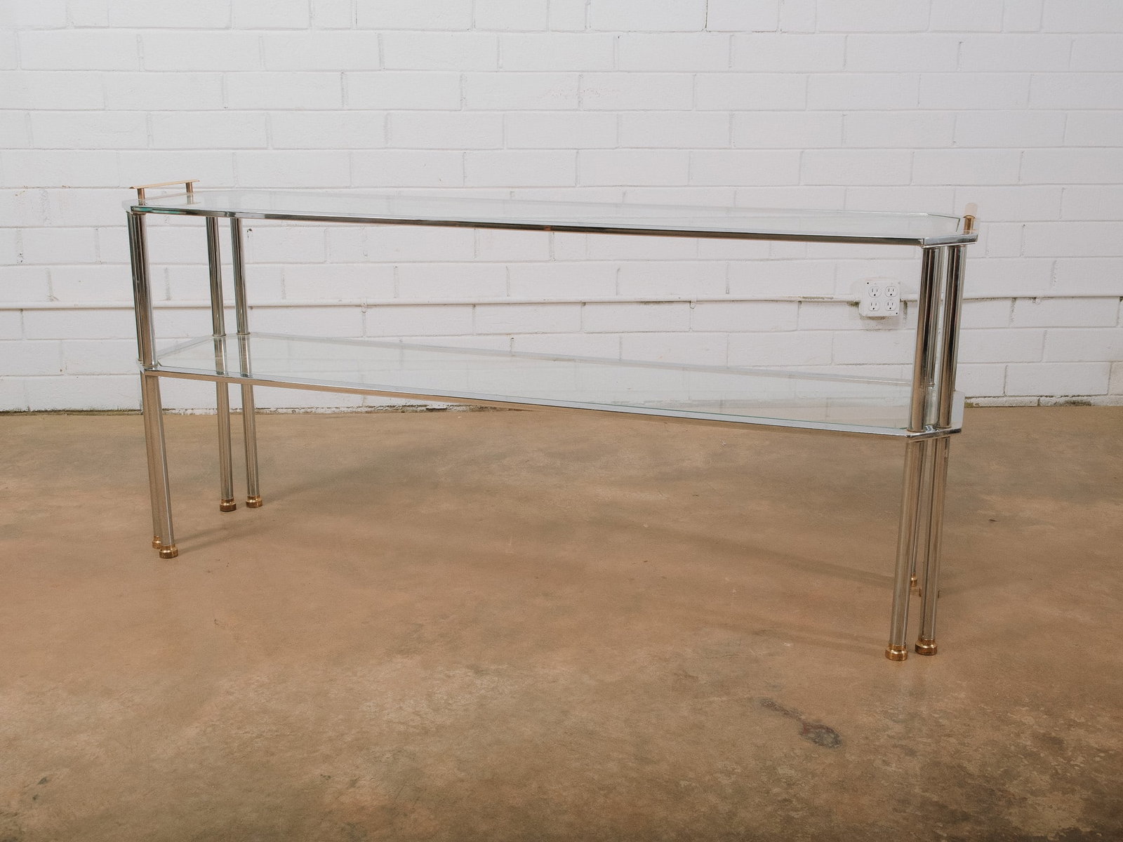 MCM Mixed Metal & Glass Console Table: Mid-century modern mixed metal and glass console table featuring a polished chrome frame accented with brass-capped feet and a clear glass lower shelf. The sleek, open design and combination of