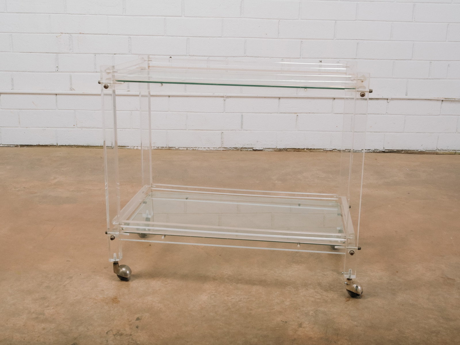 Modern Lucite Bar Cart: Modern Lucite bar cart featuring two shelves and polished metal hardware. Mounted on caster wheels for easy mobility, this versatile piece functions equally well as a bar cart, serving cart, or