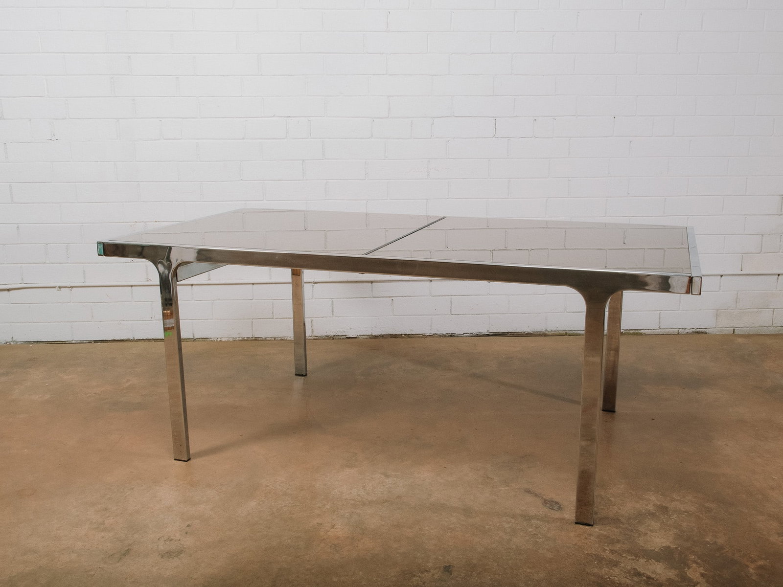 MCM Mirrored Top Dining Table: Mid-century modern dining table featuring a mirrored glass top set within a polished chrome frame. The table includes an integrated self-storing leaf that easily extends the surface for additional