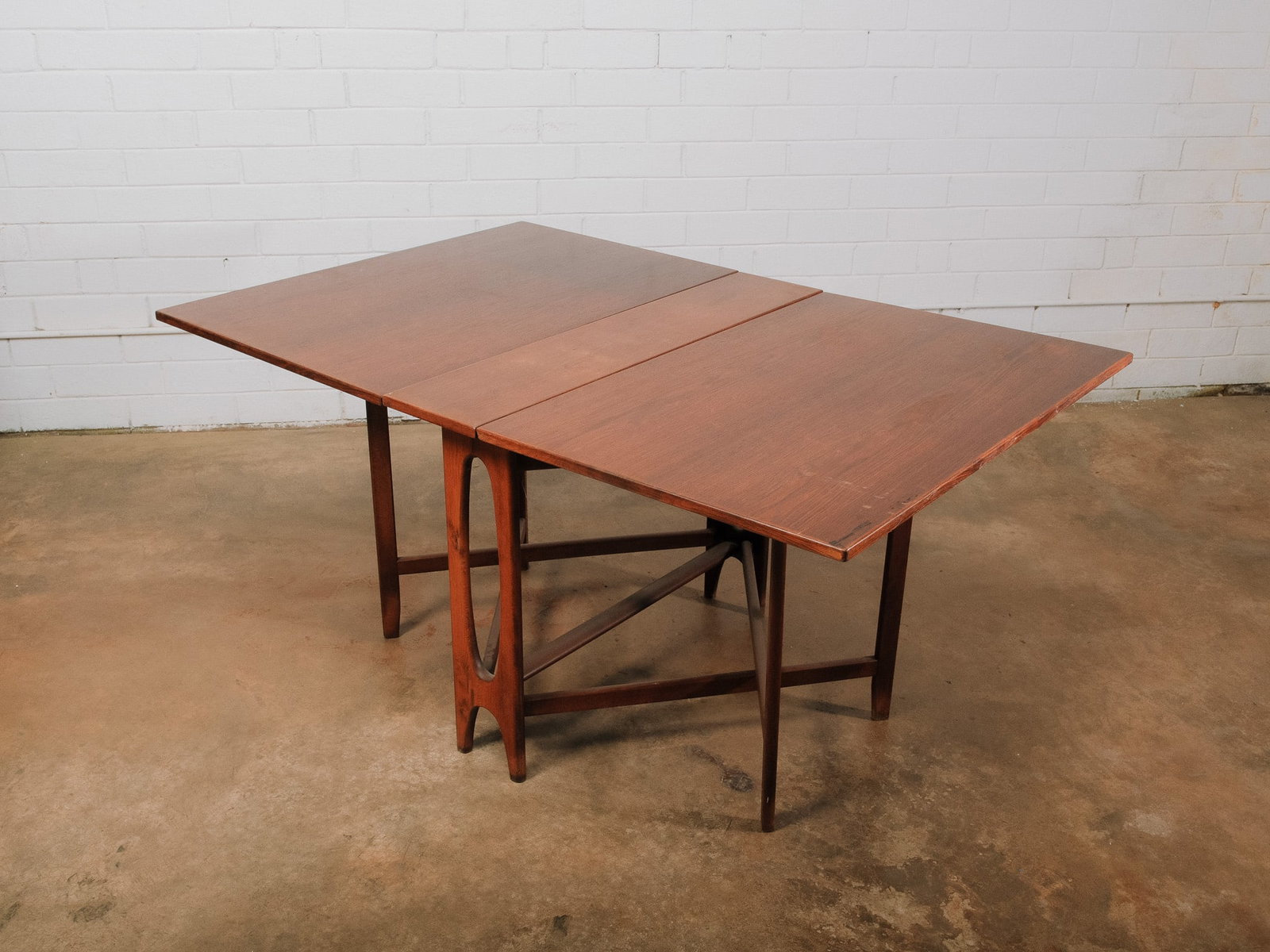 Mid-Century Drop Leaf Dining Table: Mid-century modern drop leaf dining table featuring a darker walnut-toned finish, gently tapered legs, and an elegant open pedestal base. The folding leaves allow the table to expand or collapse as ne