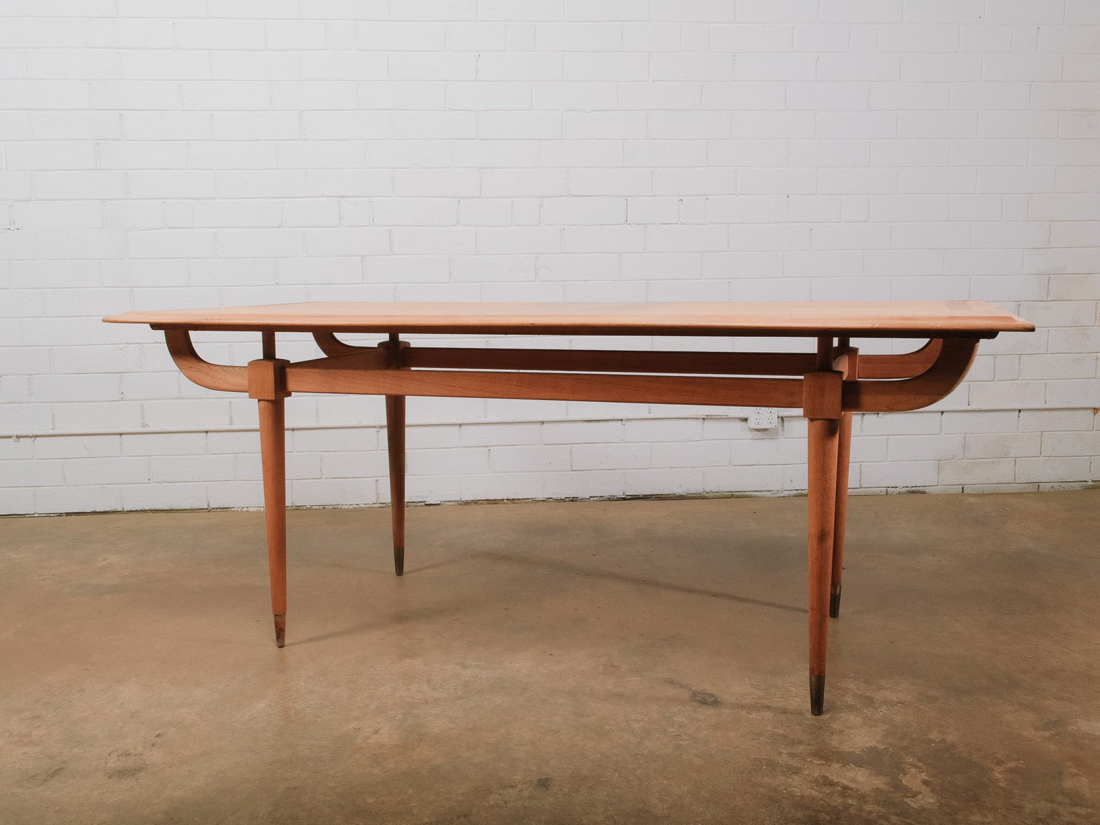 MCM Wood Dining Table: Mid-century modern dining table featuring a sculptural stretcher base with gracefully curved supports and tapered round legs accented with brass ferrules. The clean architectural lines and elegant cra
