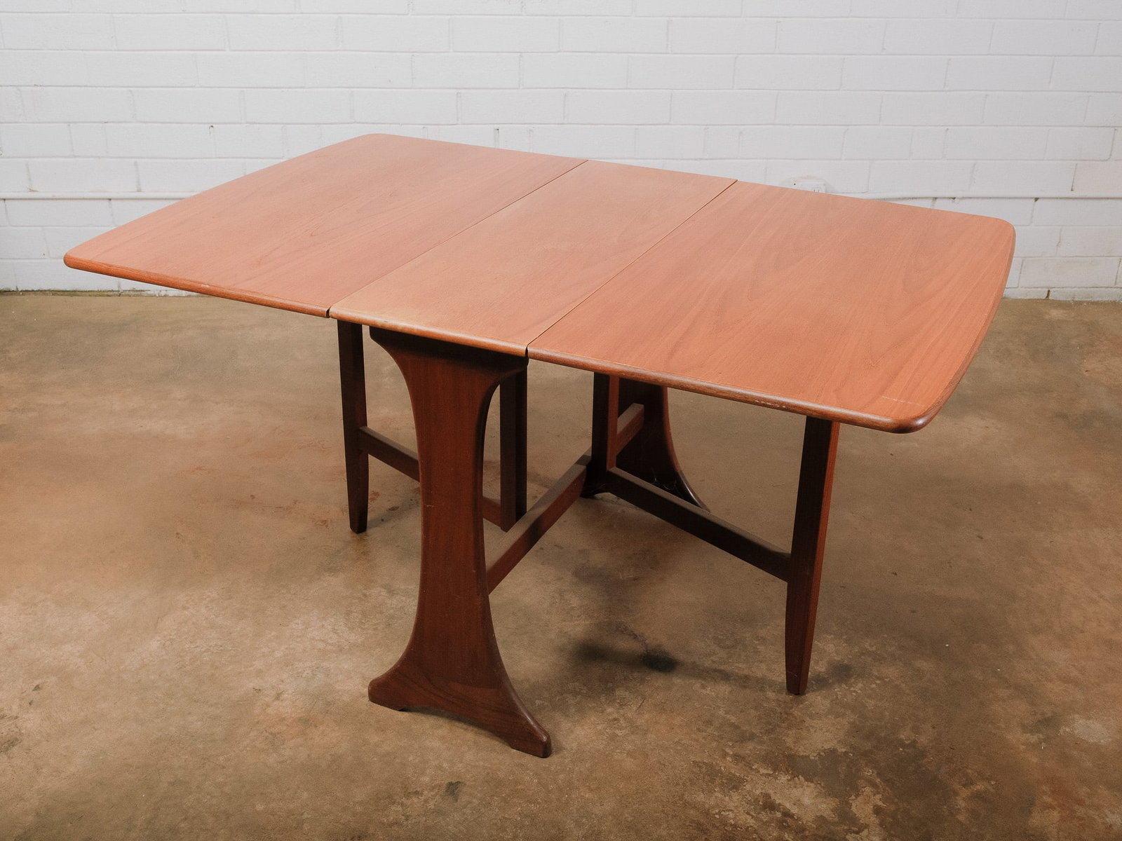 Mid-Century Drop Leaf Dining Table: Mid-century modern drop leaf dining table with clean lines and sculptural trestle-style base. Both leaves fold down to create a compact footprint, making it ideal for apartments or flexible dining