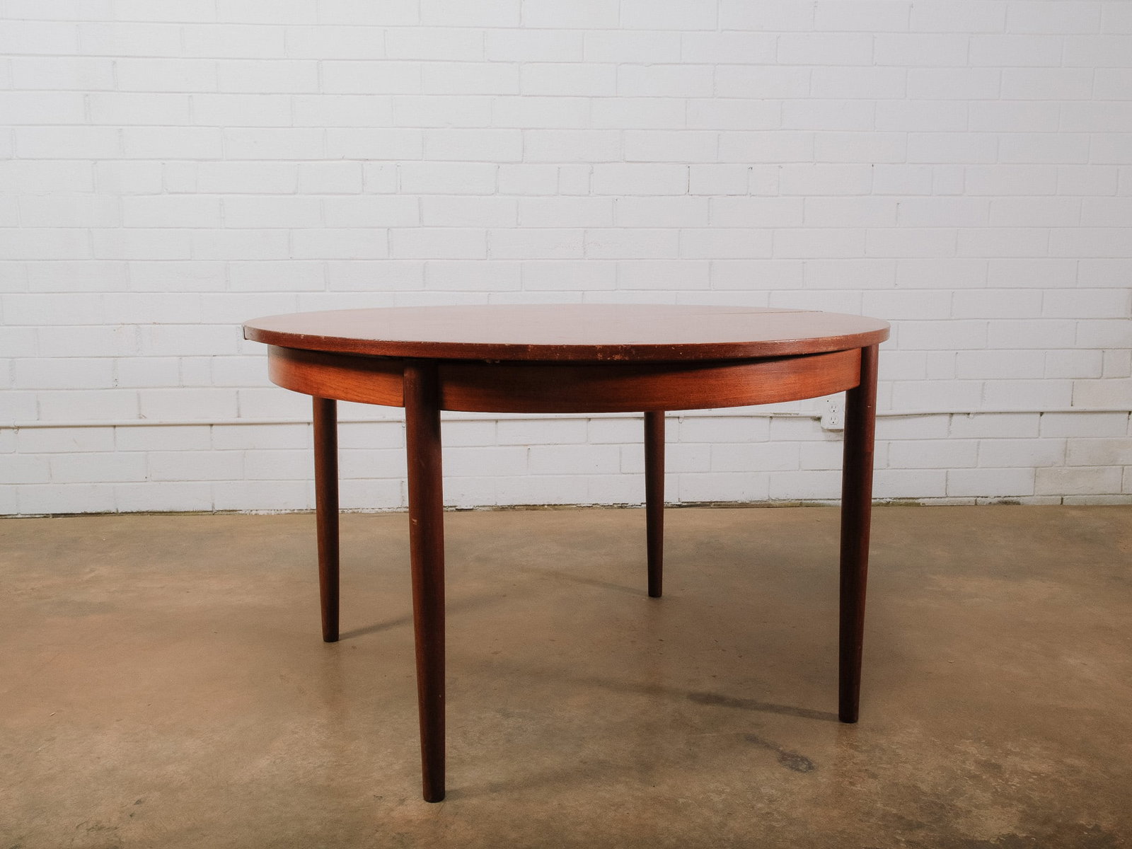Mid-Century Modern Round Expanding Dining Table: Mid-century modern round dining table featuring clean lines, tapered cylindrical legs, and a warm wood finish. The table includes an 18-inch self-storing butterfly leaf that easily expands the