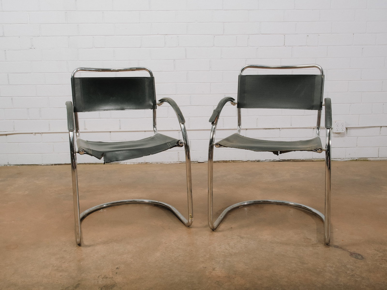 Pair of Modern Chrome Sling Armchairs: Pair of modern sling armchairs featuring polished chrome tubular frames with black leather sling backs and seats. The clean, minimalist design is complemented by integrated padded armrests, making