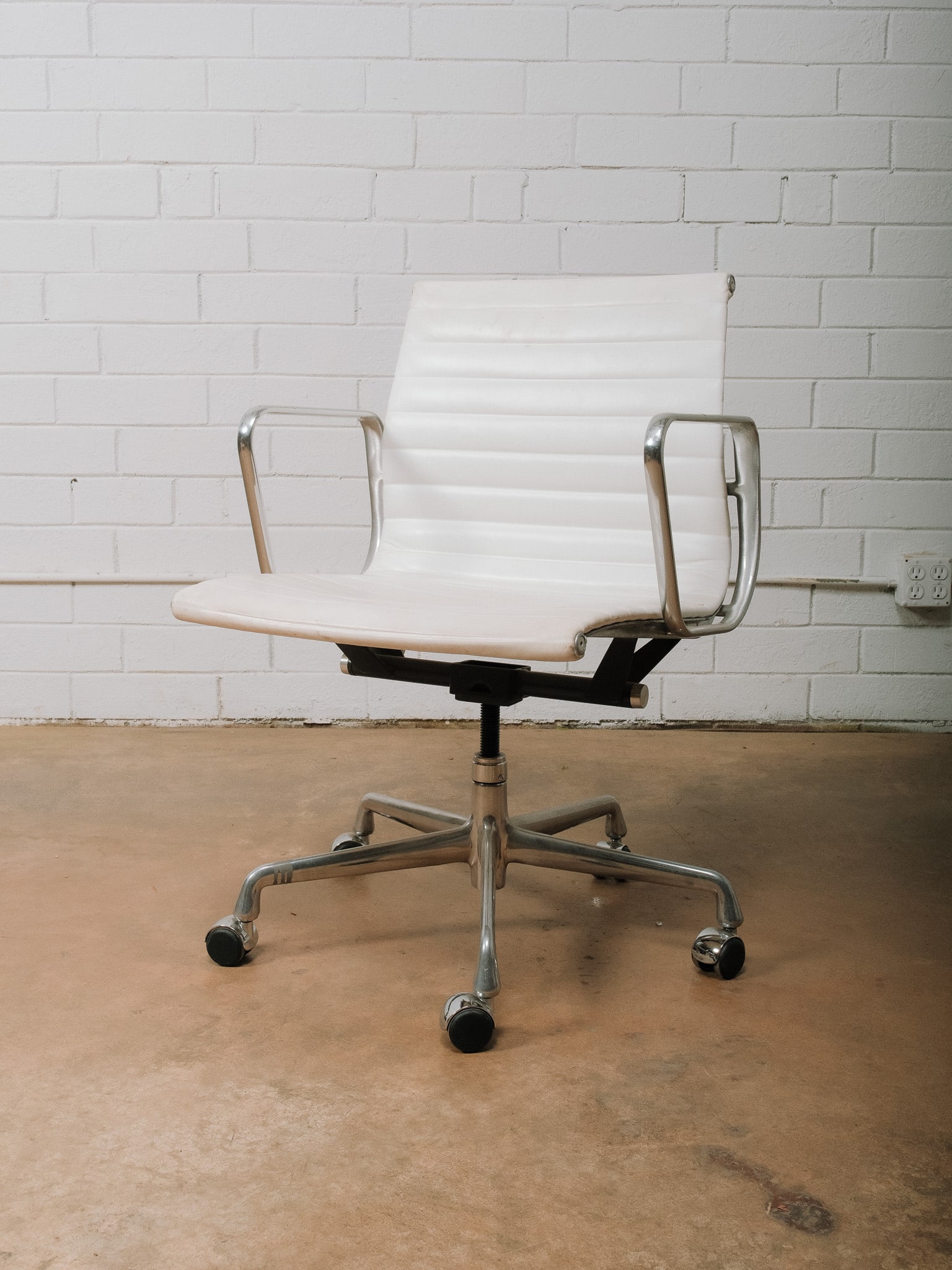 MCM White Leather Rolling Desk Chair: Mid-century modern rolling desk chair featuring a white ribbed upholstered seat and back with polished aluminum arms and a five-star caster base. The clean, timeless design offers both comfort and mob