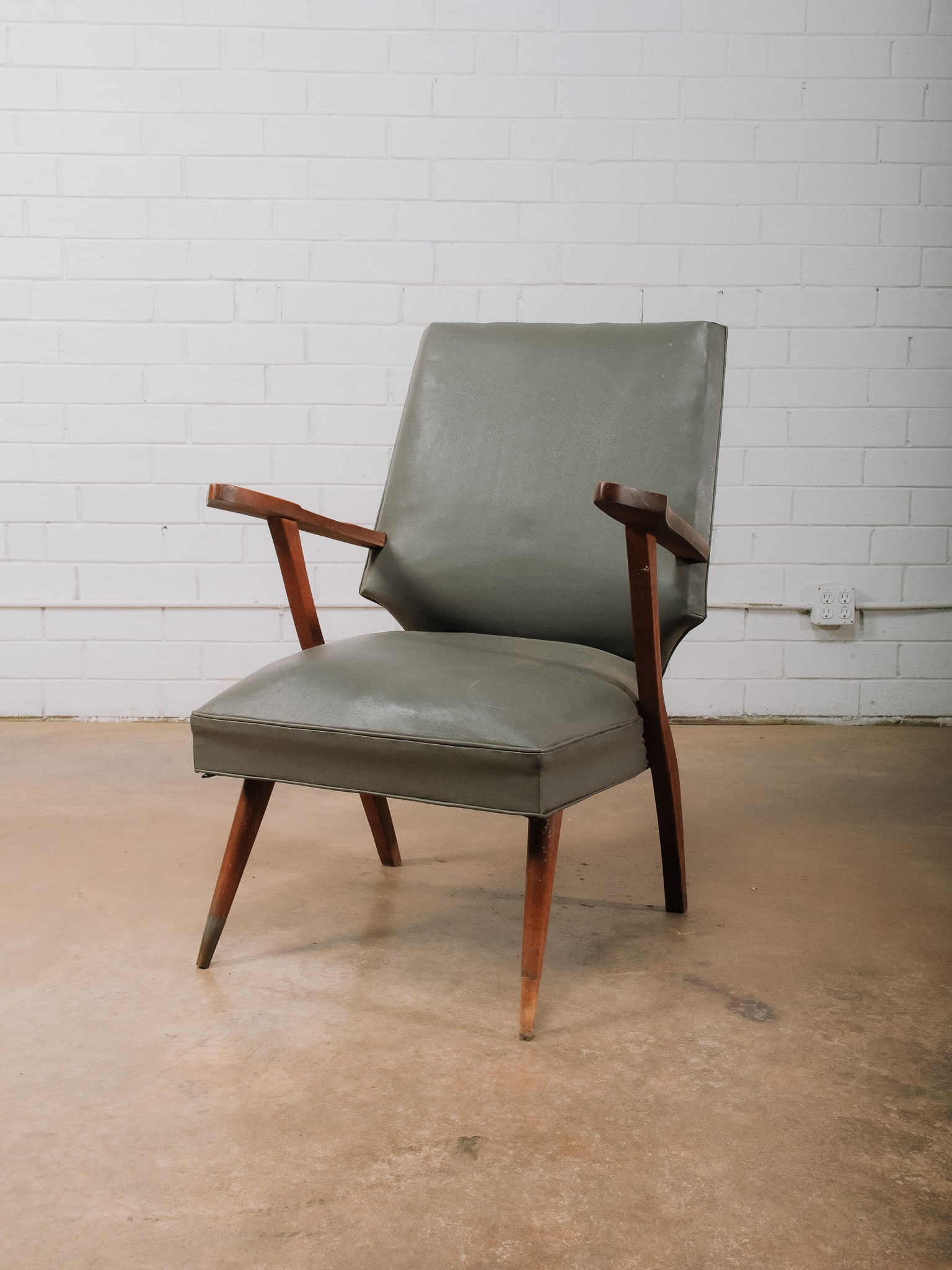 Grey MCM Accent Chair: Mid-century modern accent chair featuring a sculptural solid wood frame with angular arms, tapered legs, and gray vegan leather upholstery. The clean architectural lines and generously proportioned