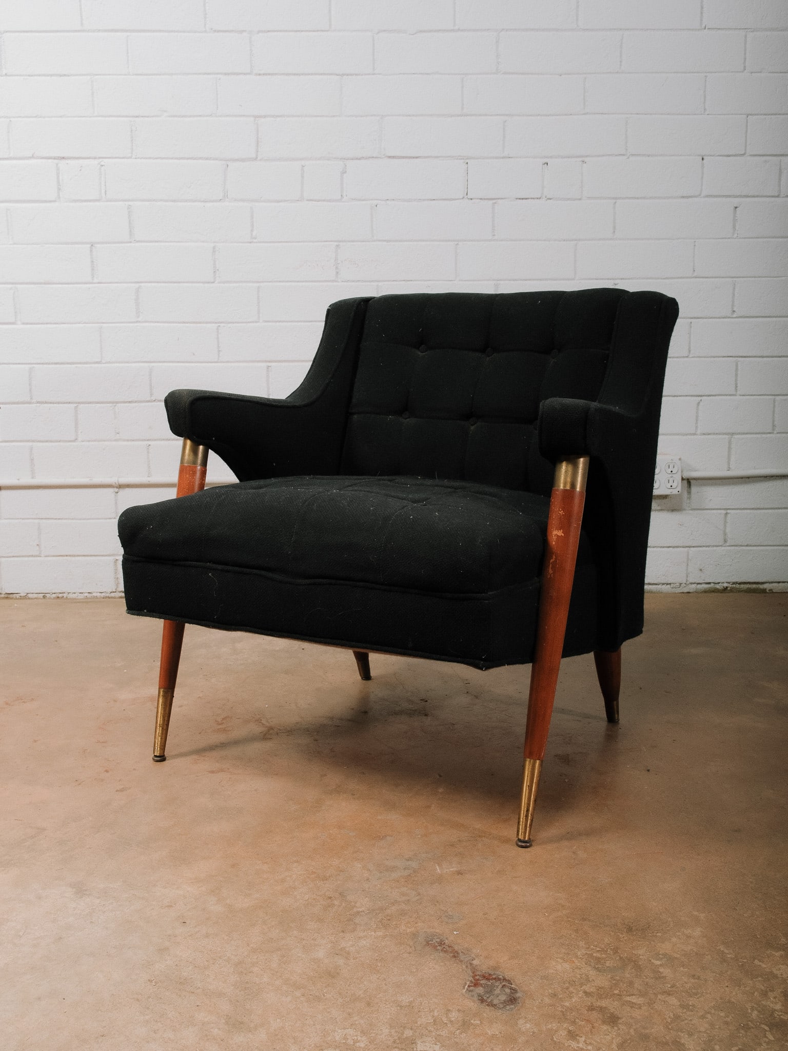 Mid-Century Tufted Arm Chair: Mid-century modern lounge chair upholstered in black fabric with a tufted back and seat, sculpted walnut arms, and brass-capped tapered legs. A comfortable accent chair with timeless styling suited