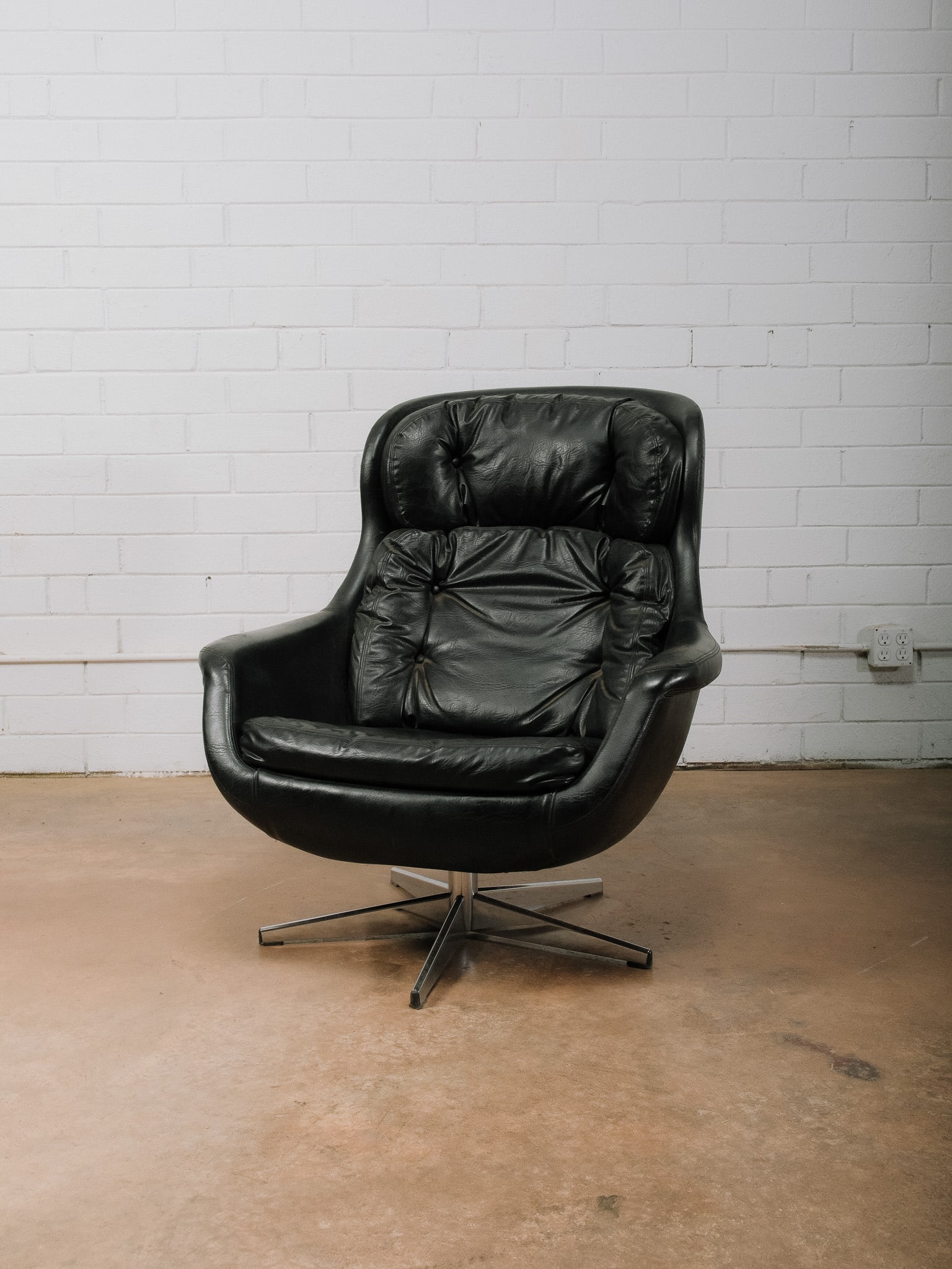 Mid-Century Modern Leather Swivel Lounge Chair: Mid-century modern lounge chair upholstered in black leather with a sculptural bucket-style seat and polished chrome four-star swivel base. Features generously padded tufted cushions, integrated arms,