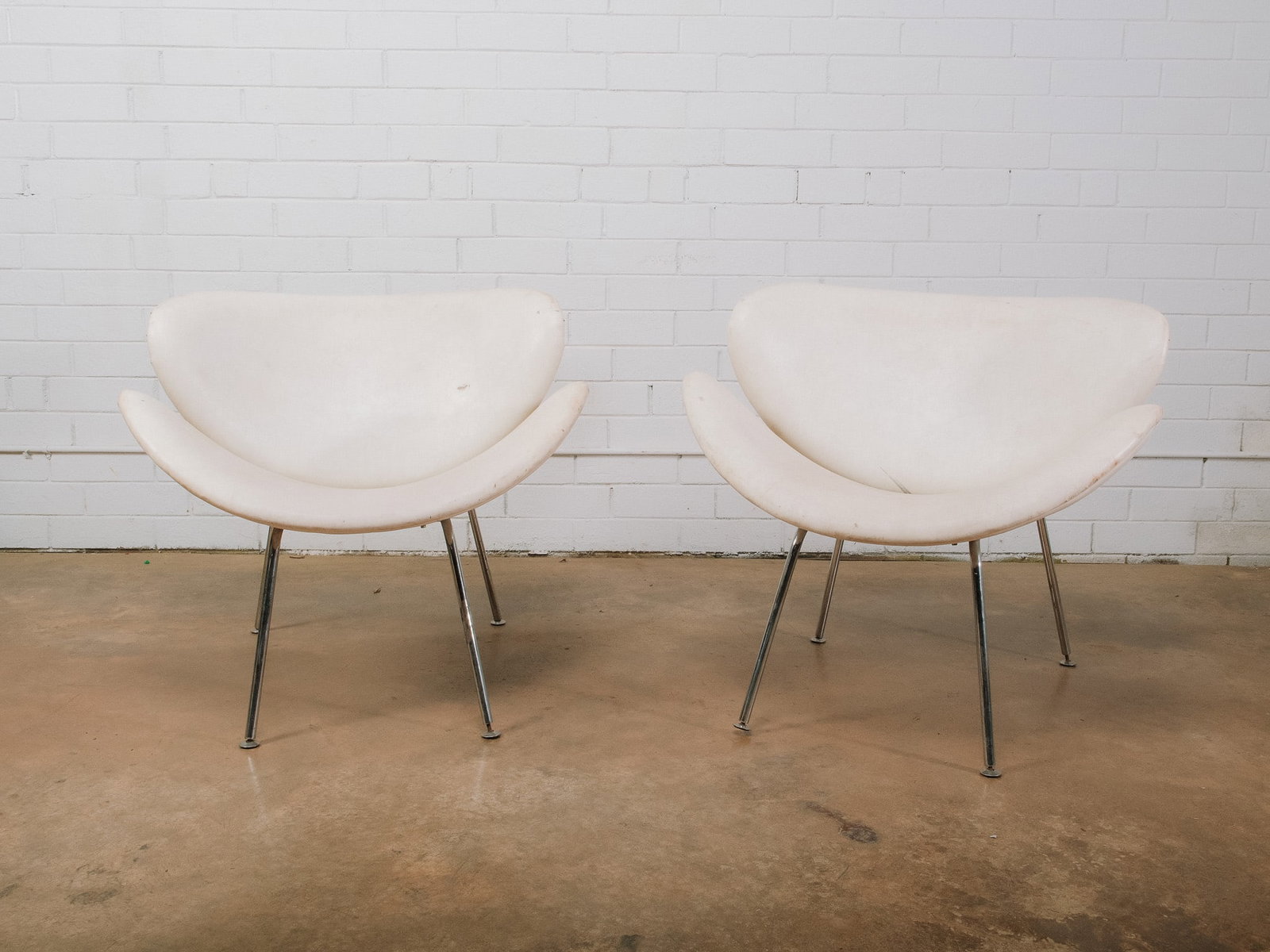 Pair of White MCM Shell Chairs: A striking pair of sculptural accent chairs featuring molded white shell seats with softly curved, organic forms. Each chair is supported by slender chromed metal legs, creating a light, modern