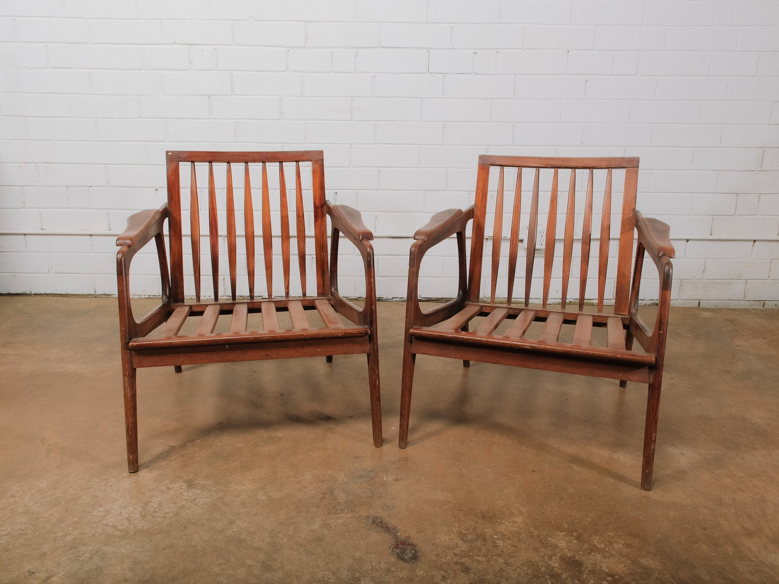 Pair of MCM Wood Armchairs: Pair of mid-century modern walnut armchairs featuring slatted backs, sculpted armrests, and elegant tapered legs. A classic design well suited for dining, office, or accent seating. Cushions not