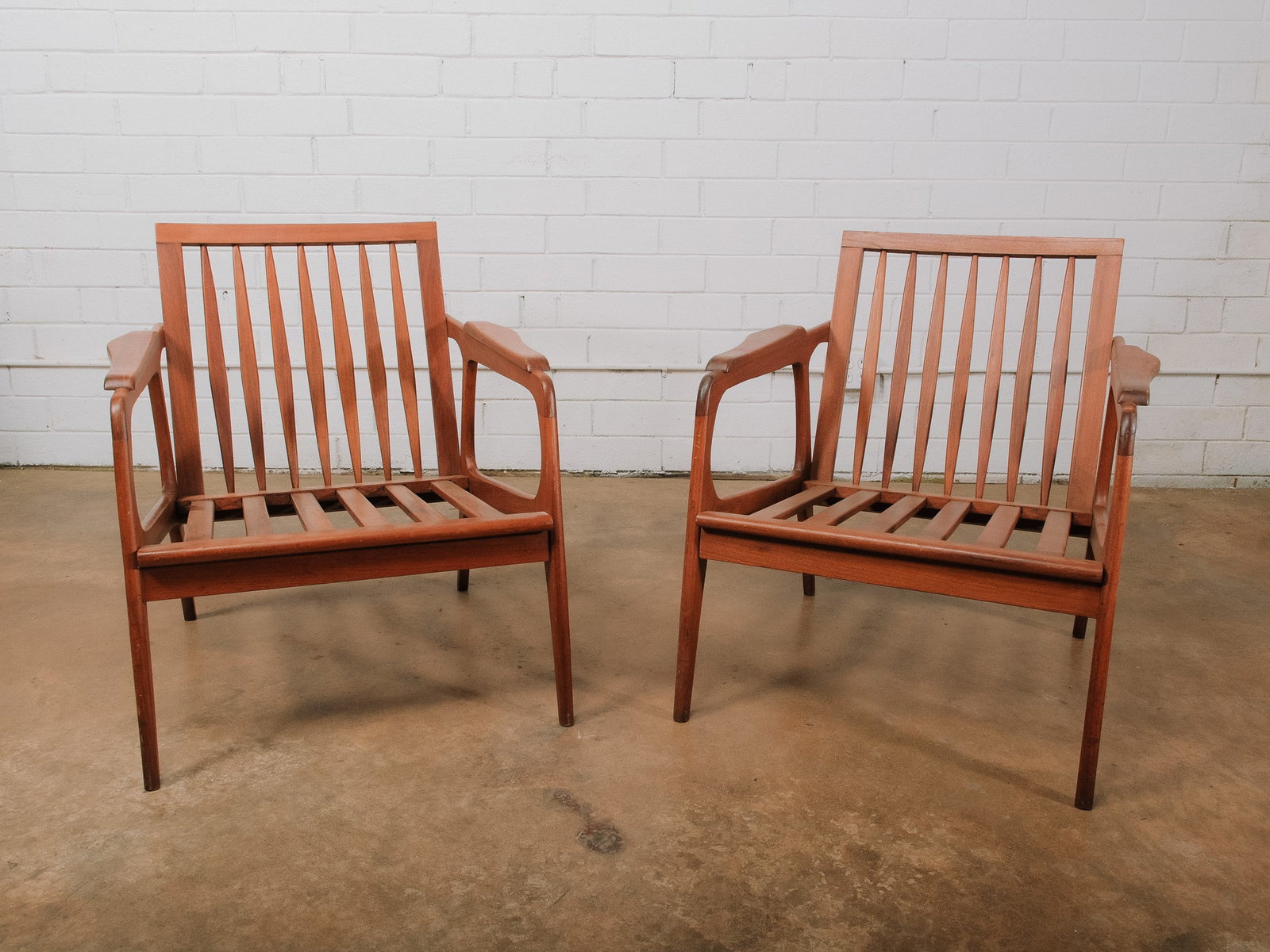 Pair of MCM Wood Armchairs: Pair of mid-century modern teak armchairs with slatted backs, sculpted arms, and clean-lined construction. Their timeless Scandinavian-inspired design makes them suitable as dining chairs, desk