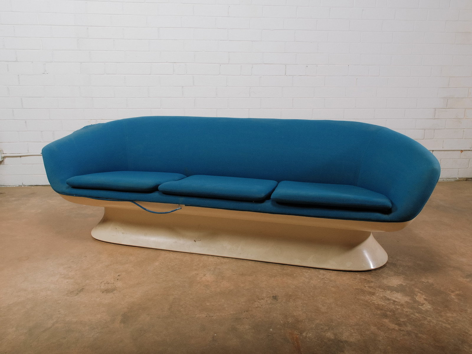Mid-Century Modern Blue Upholstered Sofa: Mid-century modern three-seat sofa featuring a sculptural white molded pedestal base and sweeping curved silhouette upholstered in vibrant blue fabric. Three loose seat cushions provide comfortable
