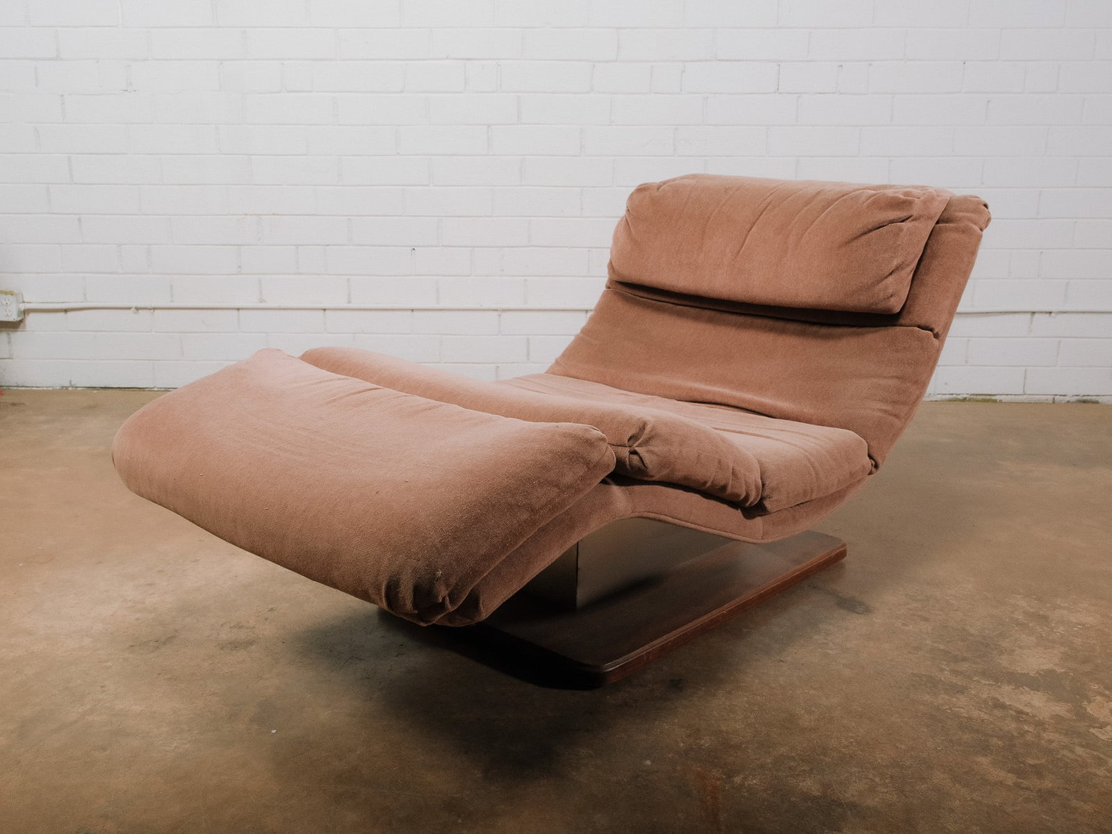 Contemporary Chaise Lounger: Contemporary chaise lounge chair featuring plush brown upholstered cushions and a sculptural wood pedestal base. The generously padded seat, integrated headrest, and extending leg rest create a comfor