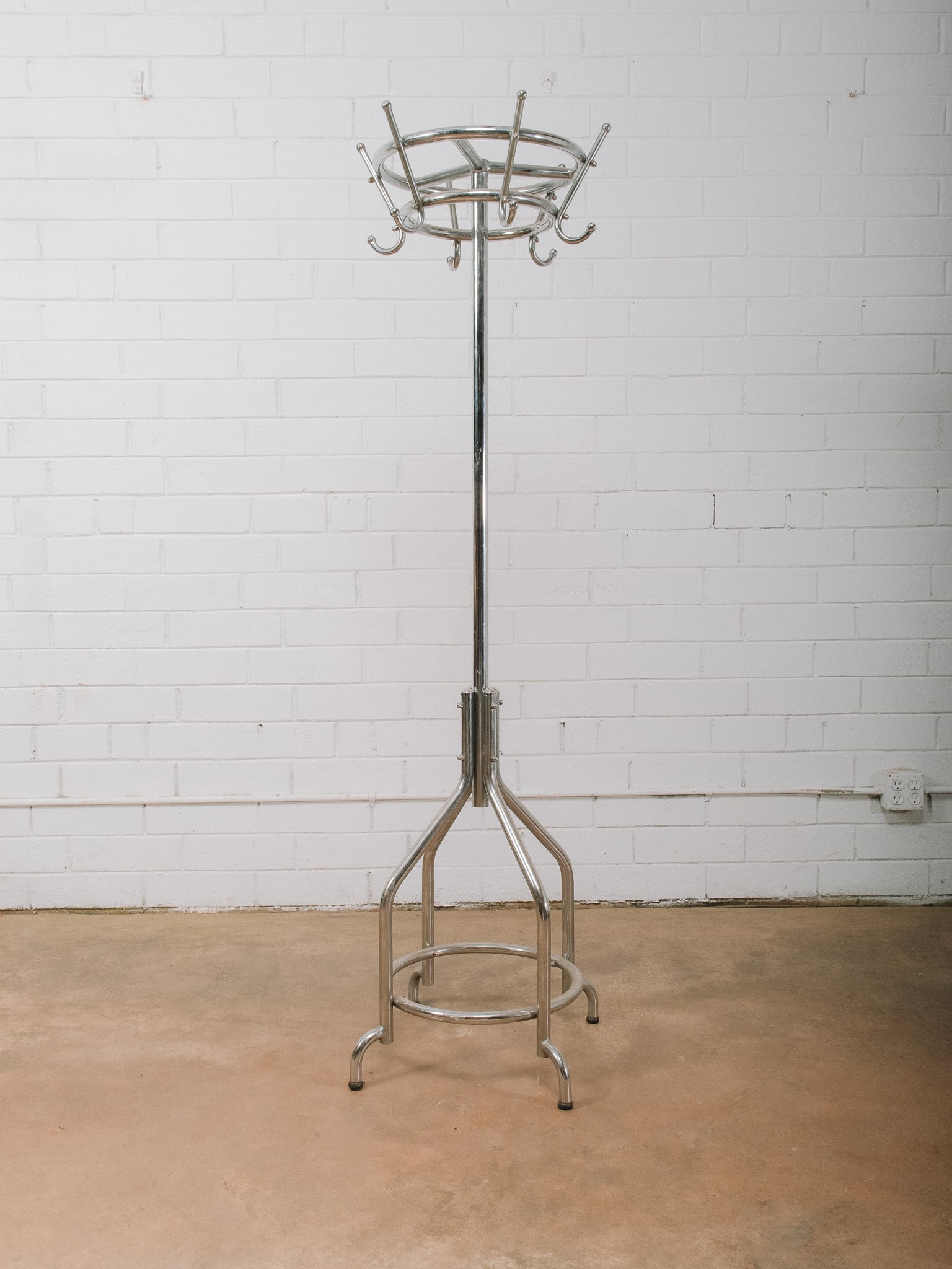 Chrome Standing Coat Rack: Freestanding chrome coat rack featuring multiple hooks for coats, hats, scarves, and bags, along with an integrated circular umbrella holder near the base. The tubular chrome construction and