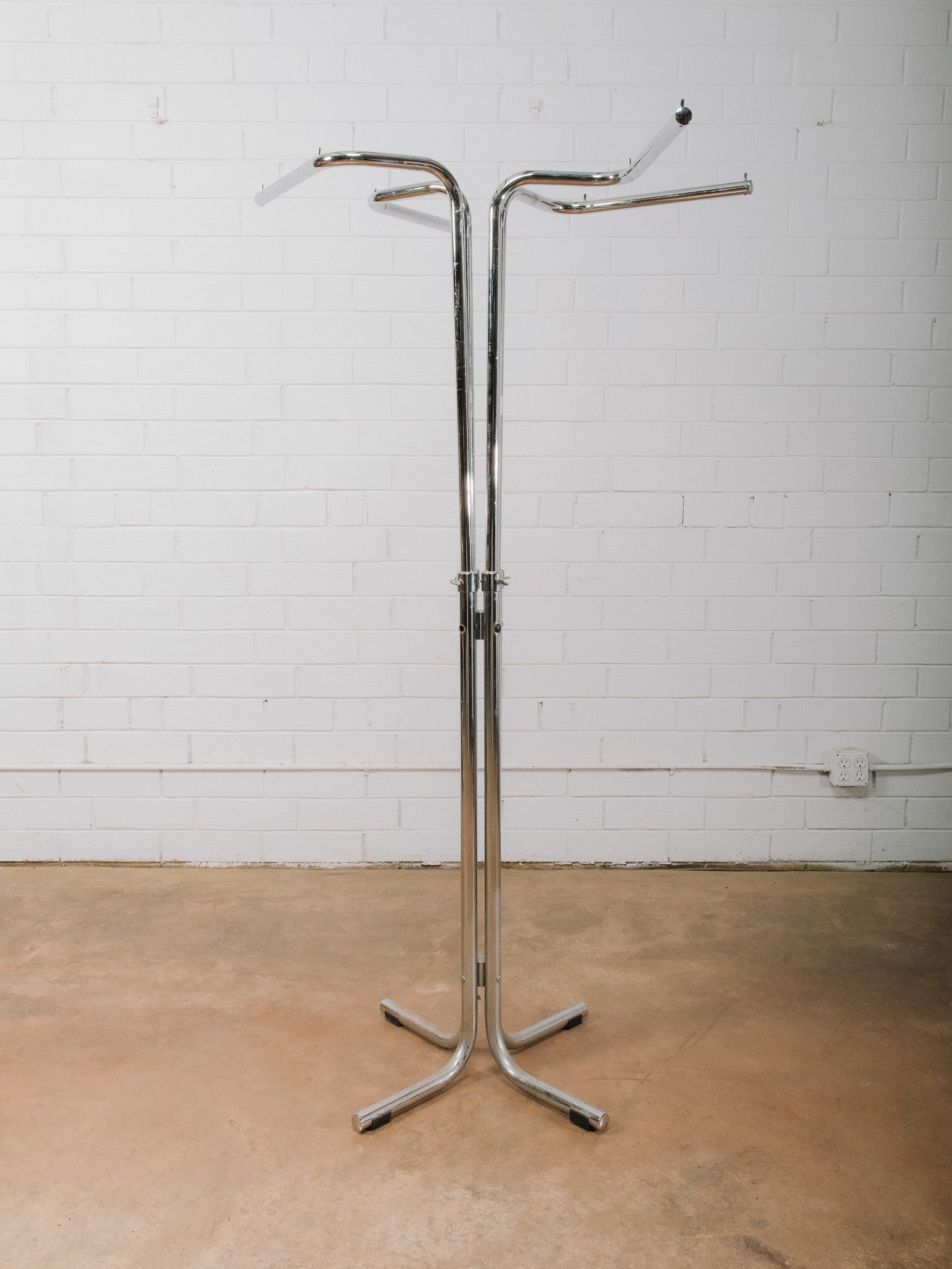 Chrome Garment Rack: Freestanding chrome garment rack featuring four cantilevered hanging arms on a sturdy four-leg base. The open, minimalist design is ideal for displaying clothing, coats, costumes, or retail