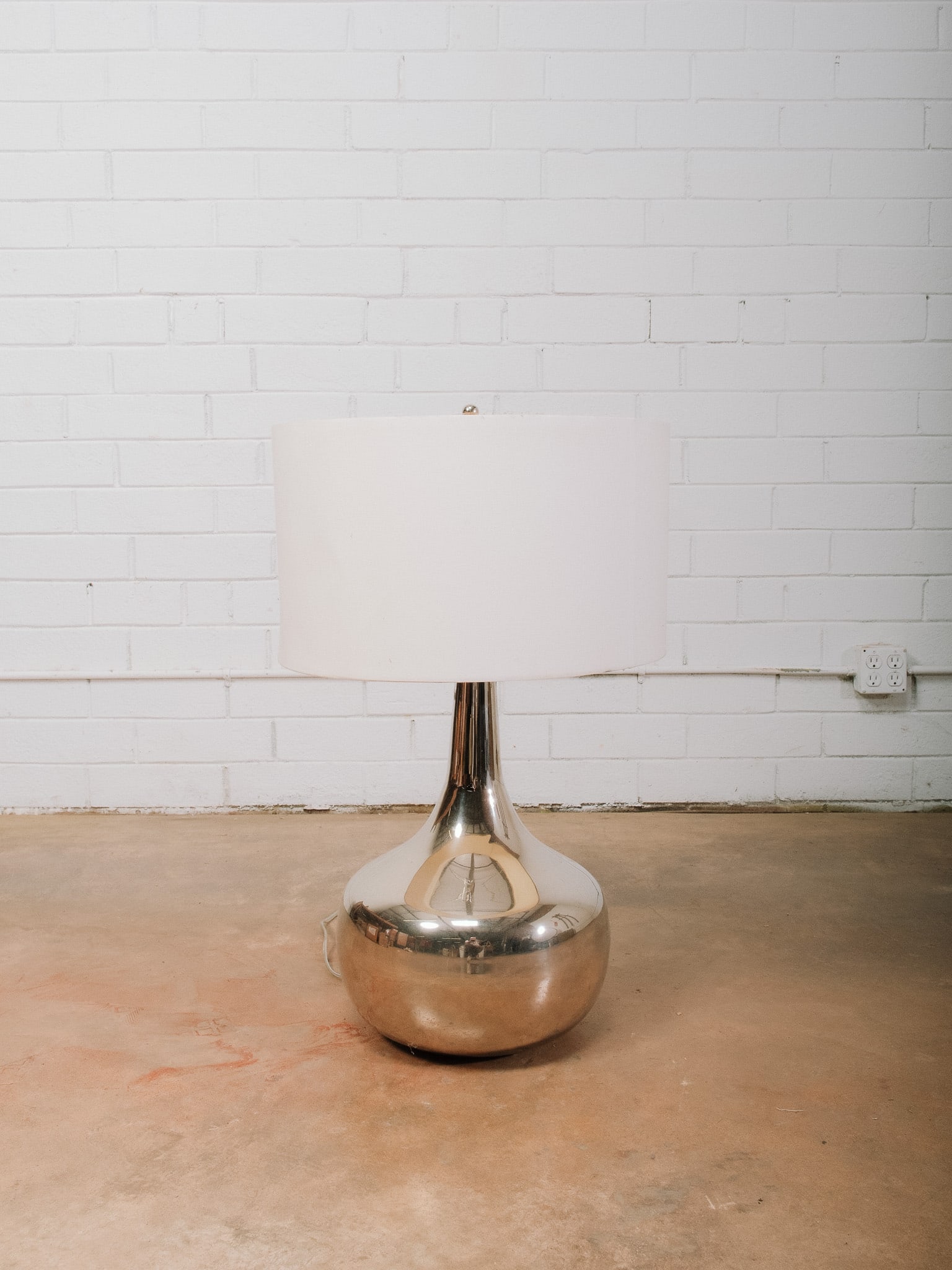 Large Chrome Table Lamp: Modern chrome table lamp with a polished teardrop-form base and oversized white drum shade. Its sleek reflective finish and minimalist silhouette make it a versatile accent for contemporary, modern,