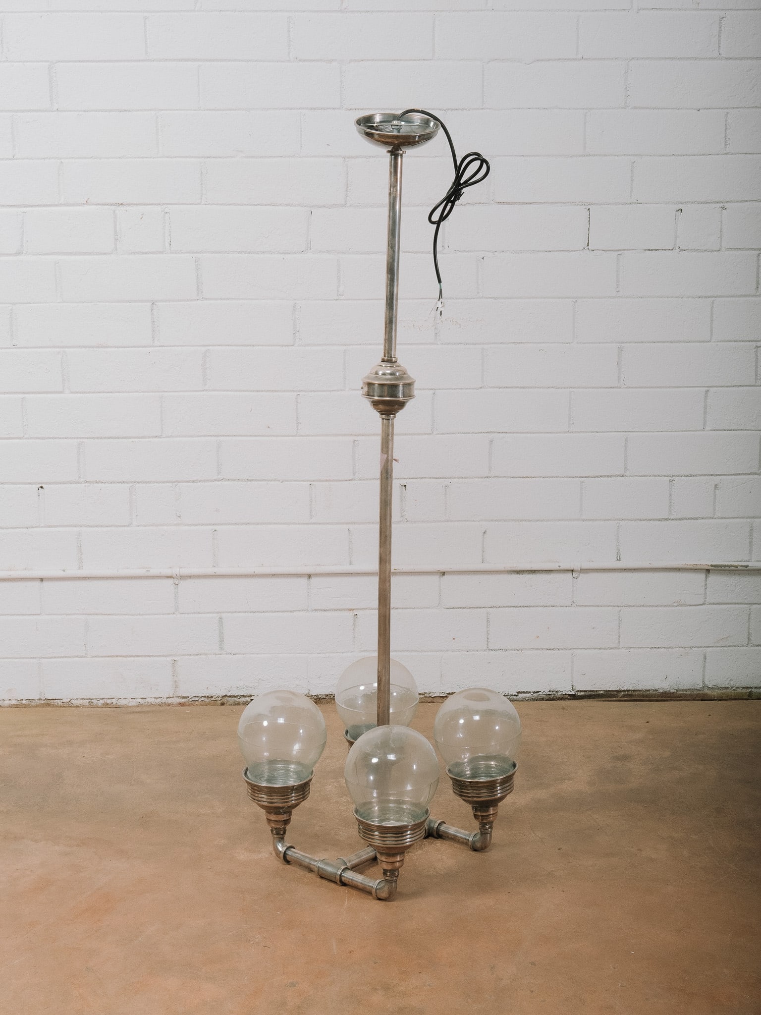 Industrial Pipe Style Four-Light Pendant Fixture: Industrial-inspired four-light pendant fixture constructed with metal pipe fittings and four globe glass shades. The sculptural open-frame design blends vintage industrial character with contemporary