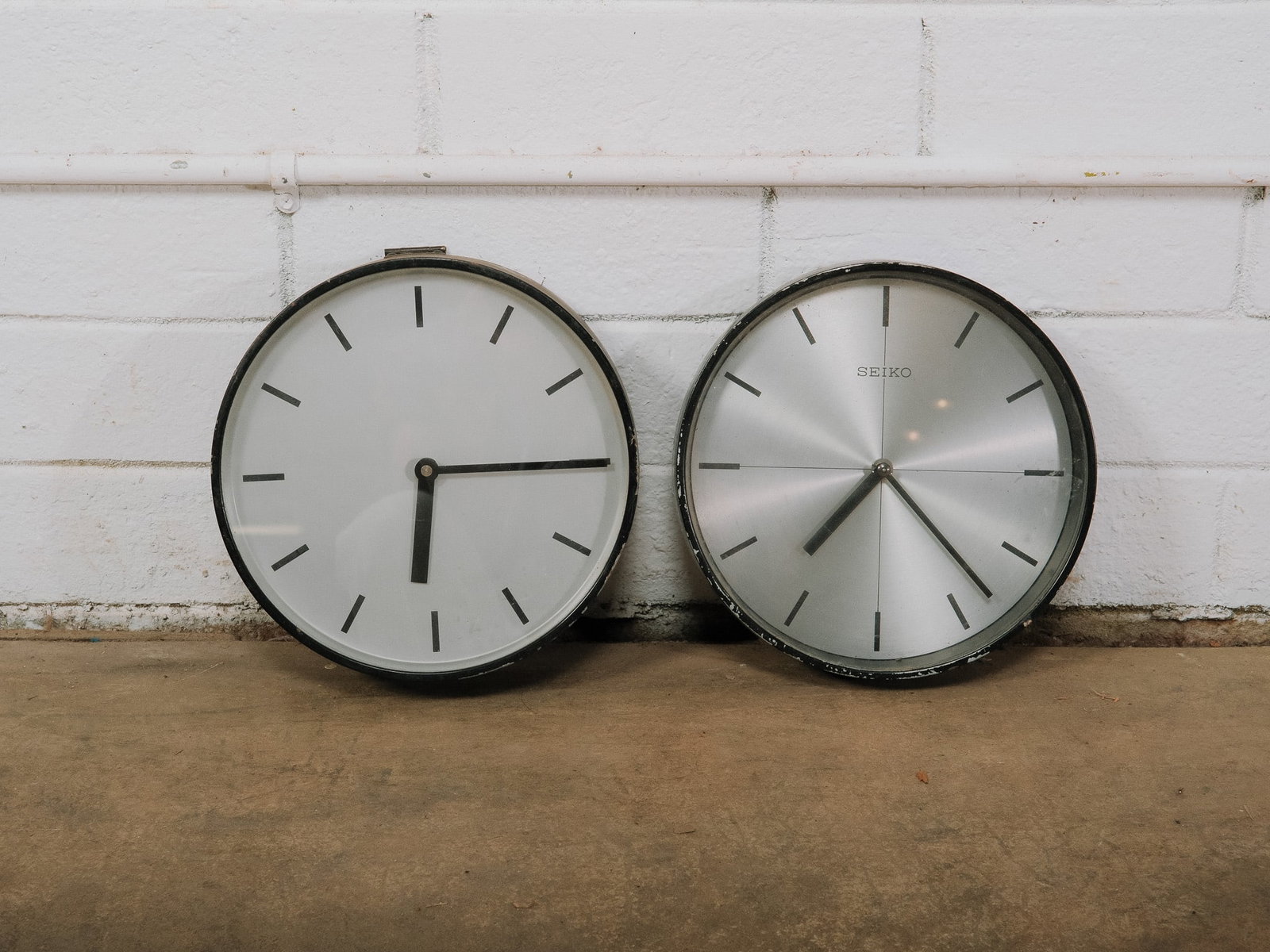 Pair of Black Seiko Wall Clocks: Pair of Seiko wall clocks featuring brushed aluminum dials with minimalist black hour markers and slim hands. Both clocks have a black frame, offering a clean modern aesthetic suitable for home or