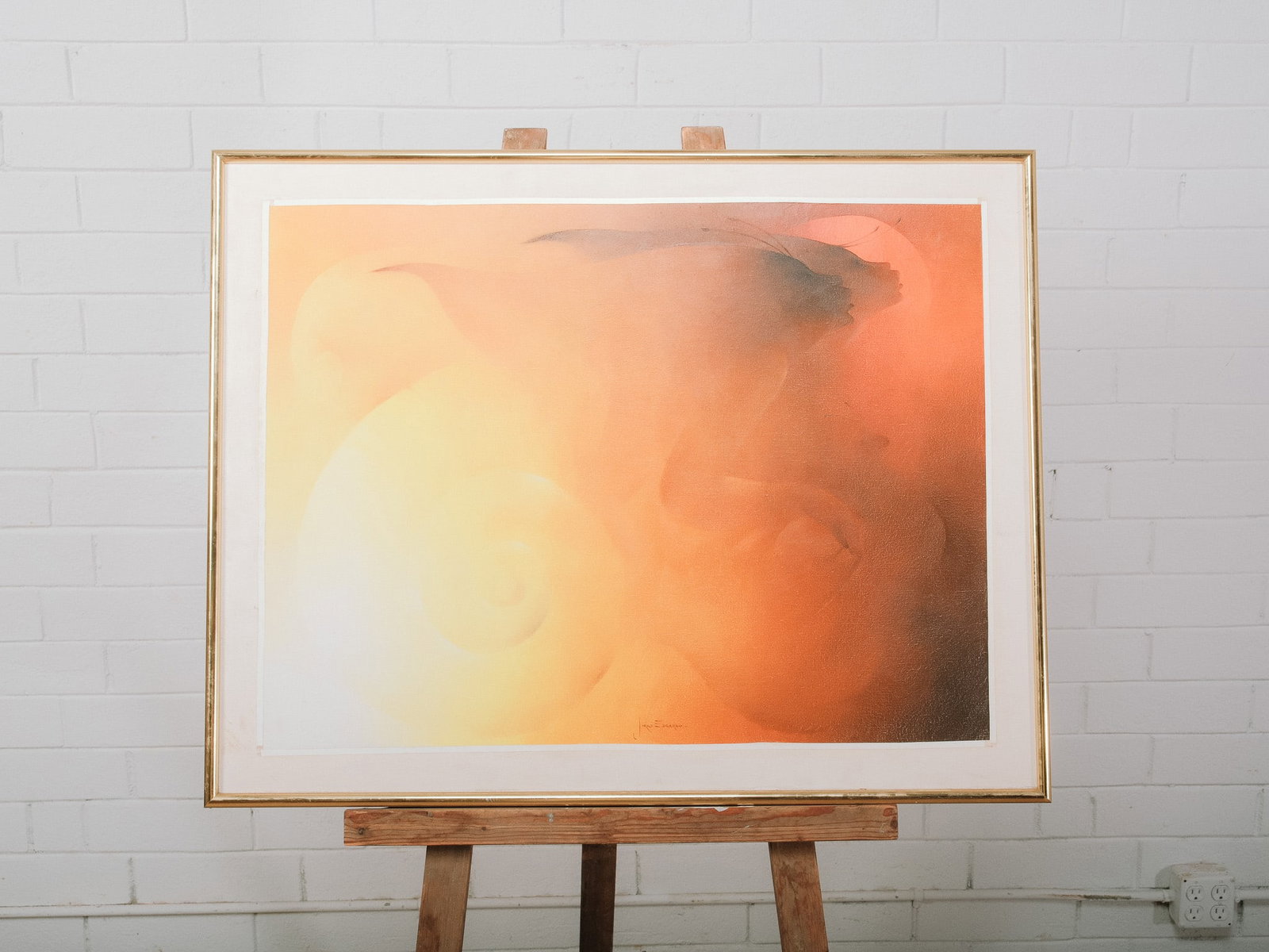 Abstract Composition in Gold Frame: Abstract composition in warm amber, peach, and charcoal tones with expressive layered brushwork and soft gradients. Signed lower center and presented under glass in a gold-tone frame with white