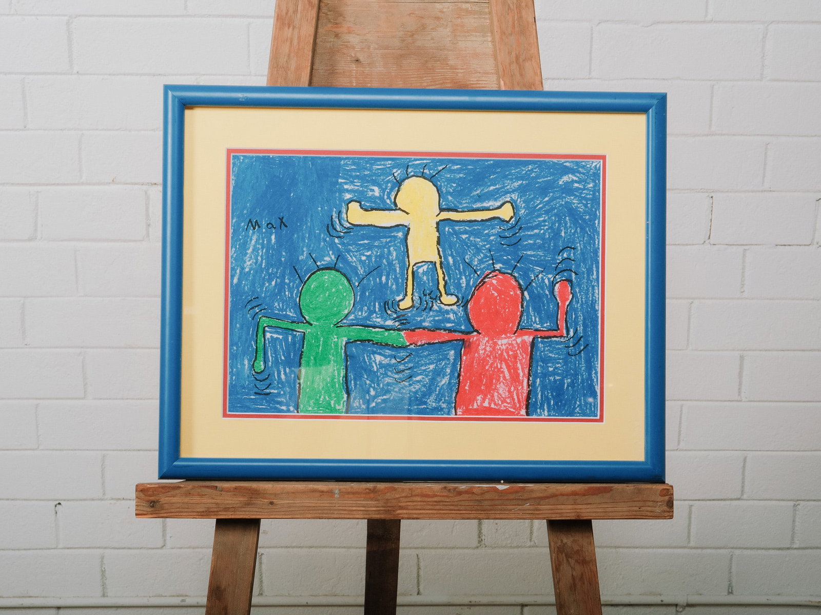 Framed Child's Folk Art Drawing: Framed folk art-style drawing depicting three colorful figures against a blue background. Signed "Max" upper left and presented in a blue-painted wood frame with contrasting mat.Approximate