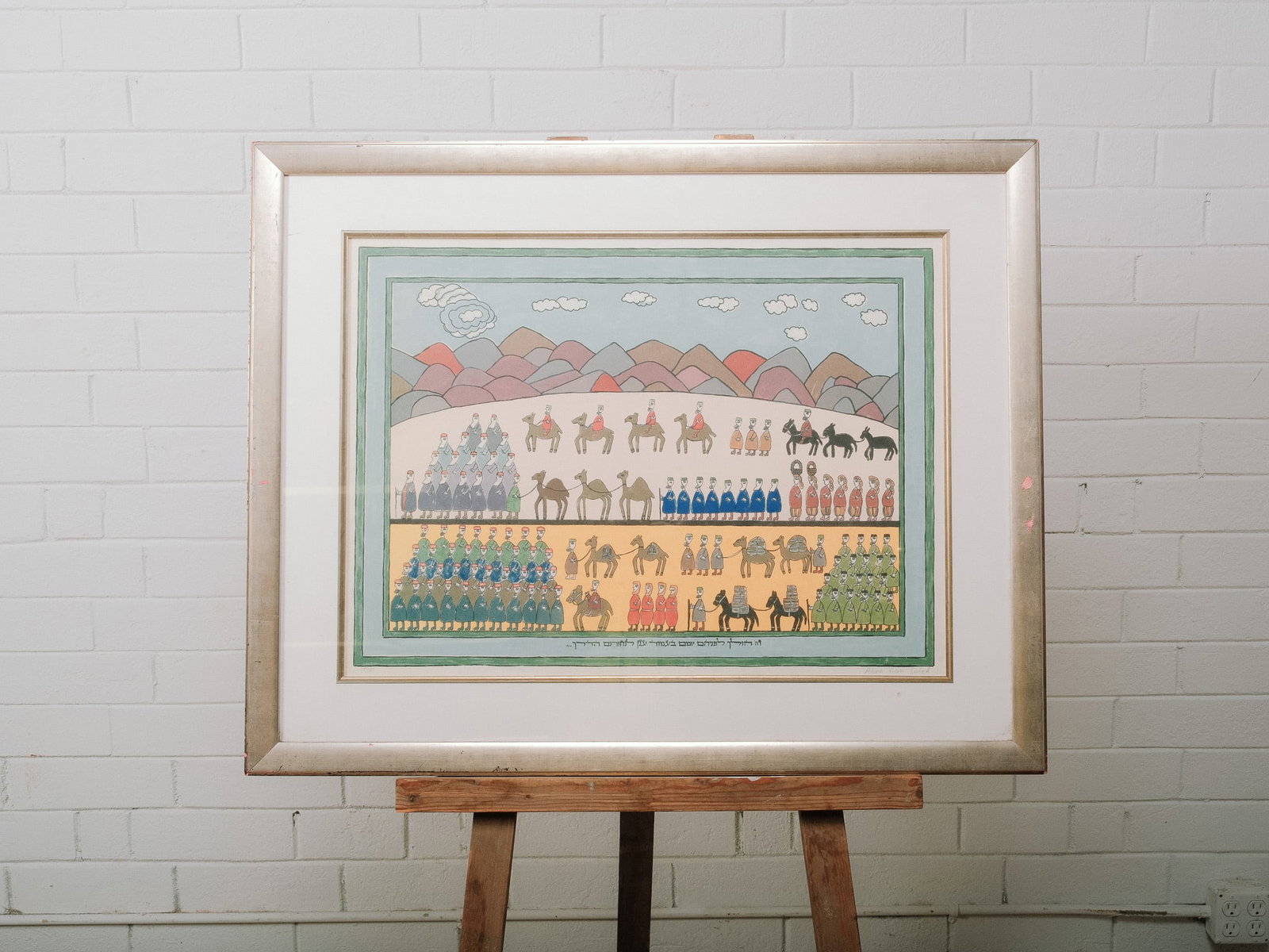Framed Judaica Folk Art Print: Framed folk art print depicting ceremonial figures, animals, and desert landscape with Hebrew text below the image. Matted and housed in a silver-tone frame under glass.Approximate Dimensions: 29"h x