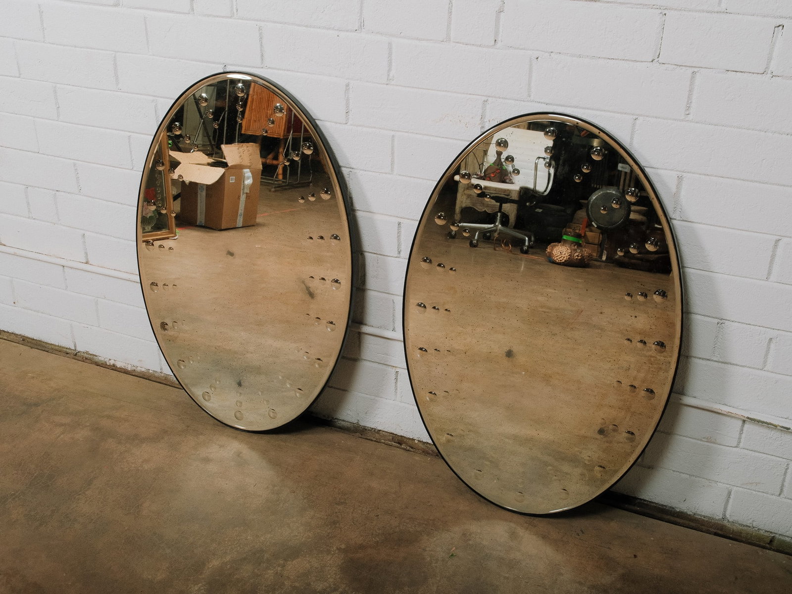 Pair of Oval Mirrors: Pair of contemporary beveled oval wall mirrors featuring polished mirrored glass with decorative raised circular accents around the perimeter. Their clean, modern design makes them ideal for