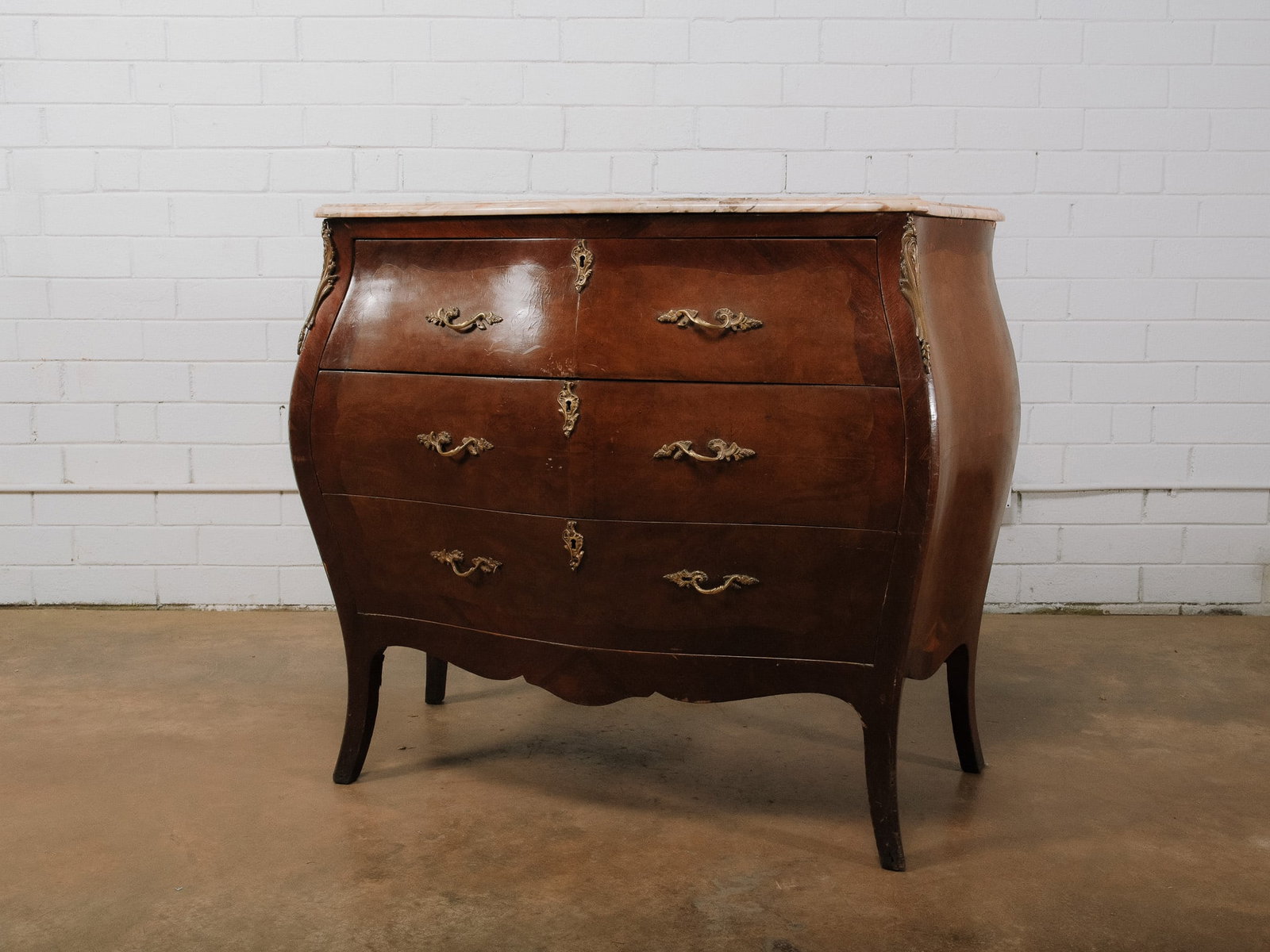 Marble Top Bombe Chest: French Provincial-style bombe chest with a shaped marble top over three serpentine drawers. The case features a warm wood finish accented by cast brass hardware and decorative mounts, standing on grac