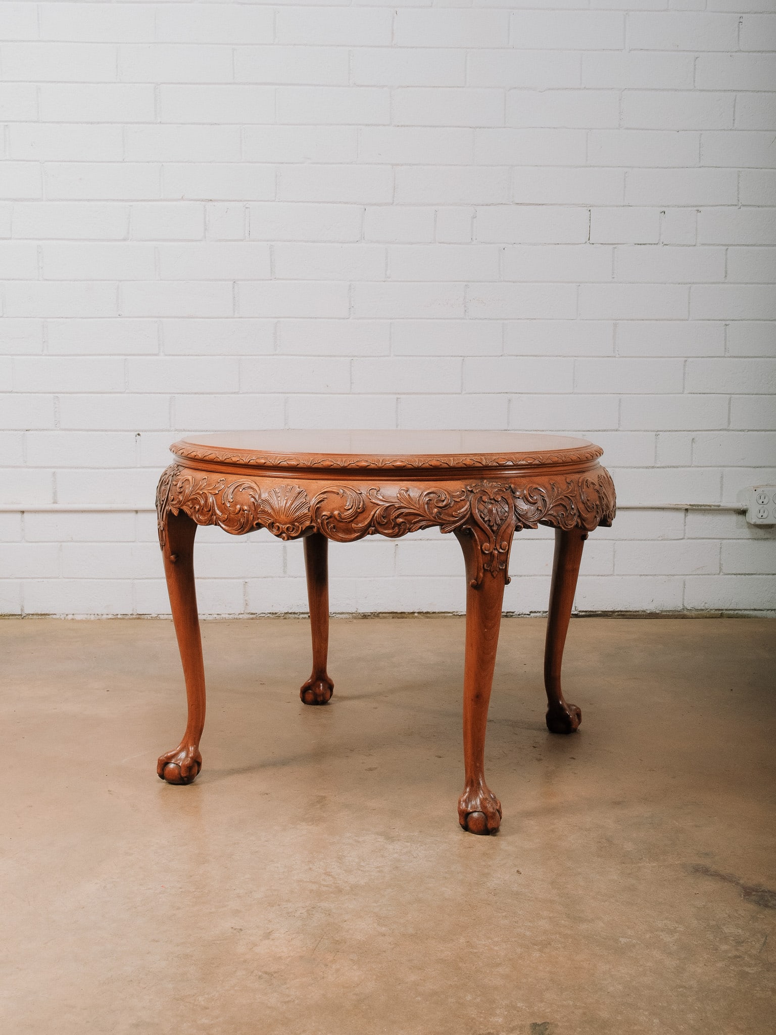 Carved Round Accent Table: Carved round wood coffee table featuring an ornate scrolling apron and ball-and-claw feet. Traditional styling with a warm wood finish.Approximate Dimensions: 22.5"h x 32"w x 32"d