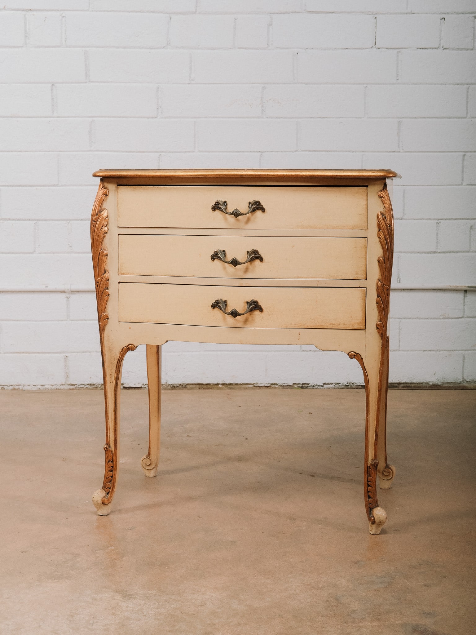 French Provincial Three-Drawer Chest: French Provincial three-drawer chest featuring a cream painted finish with gilt accents, carved foliate detailing, cabriole legs, and decorative metal drawer pulls. Its tall, compact proportions make