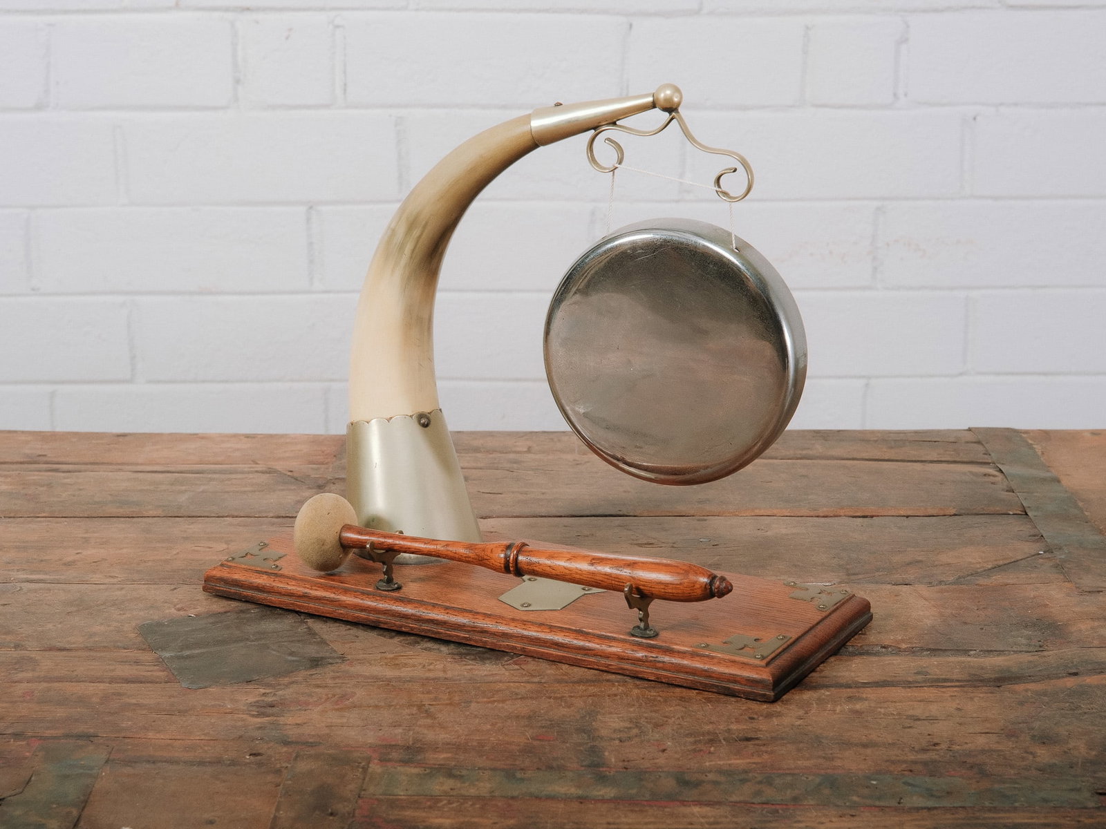 Functional Table Top Gong: Decorative tabletop gong featuring a suspended brass gong mounted beneath a curved horn-style support with metal accents on a wooden base. Includes the original wooden striker and produces a clear rin