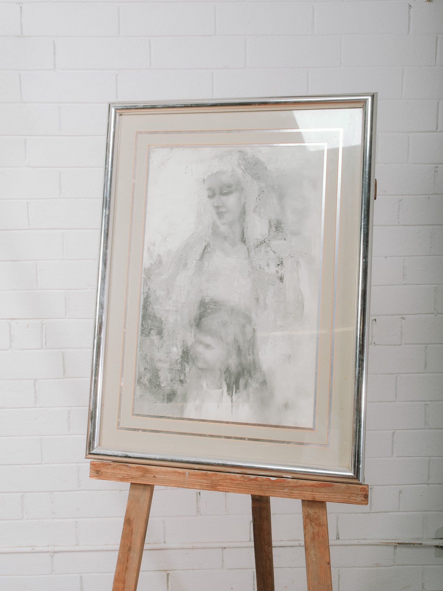 Framed Figural Artwork: Framed monochromatic artwork depicting a serene female figure with a child in a soft, ethereal composition. Presented beneath a double mat in a silver-tone frame, the gentle palette and expressive