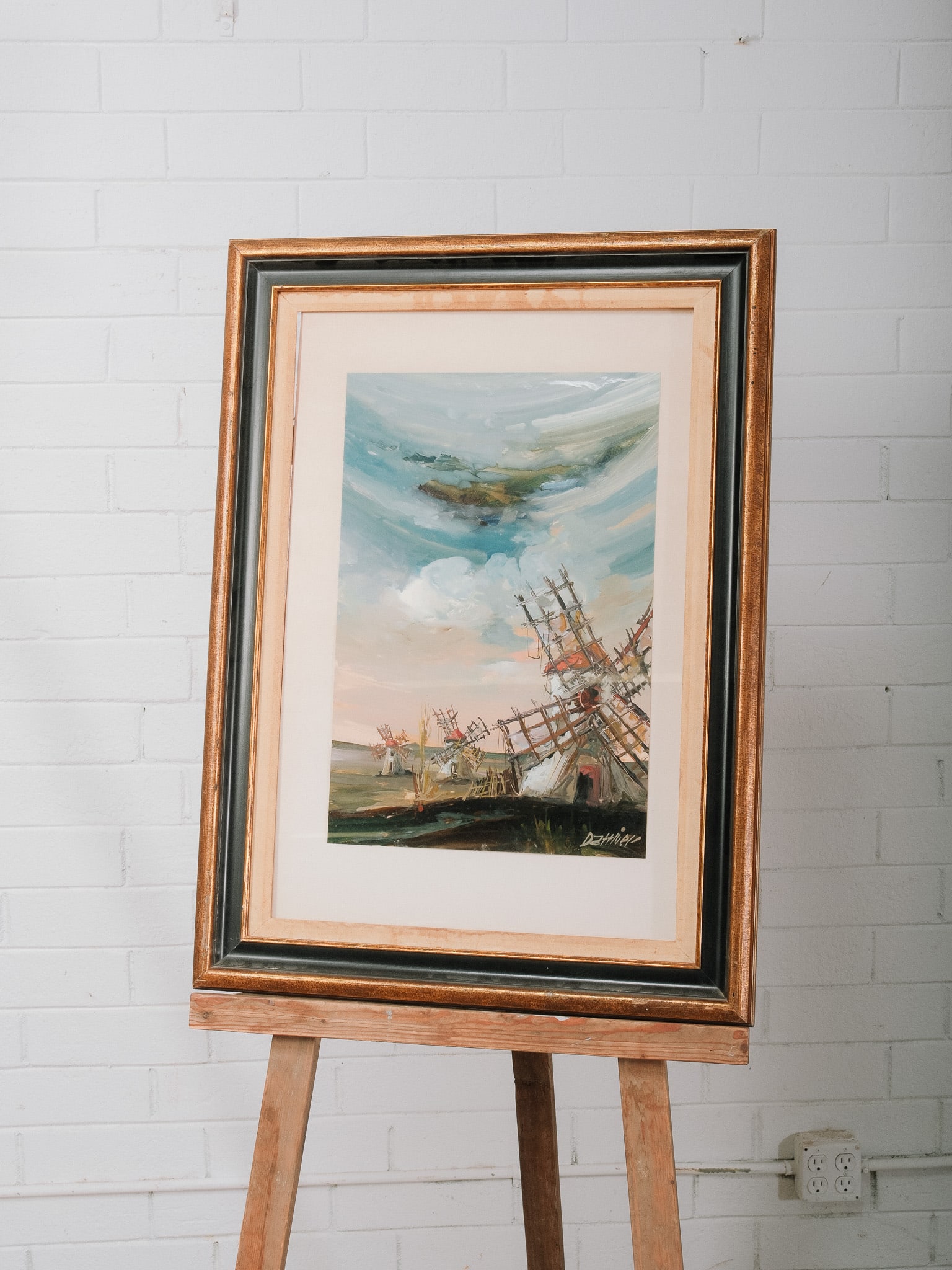 Framed Coastal Landscape Painting: Framed coastal landscape painting depicting a group of traditional windmills beneath an expressive sky rendered in loose, impressionist brushstrokes. Presented in a wide mat with a decorative wood
