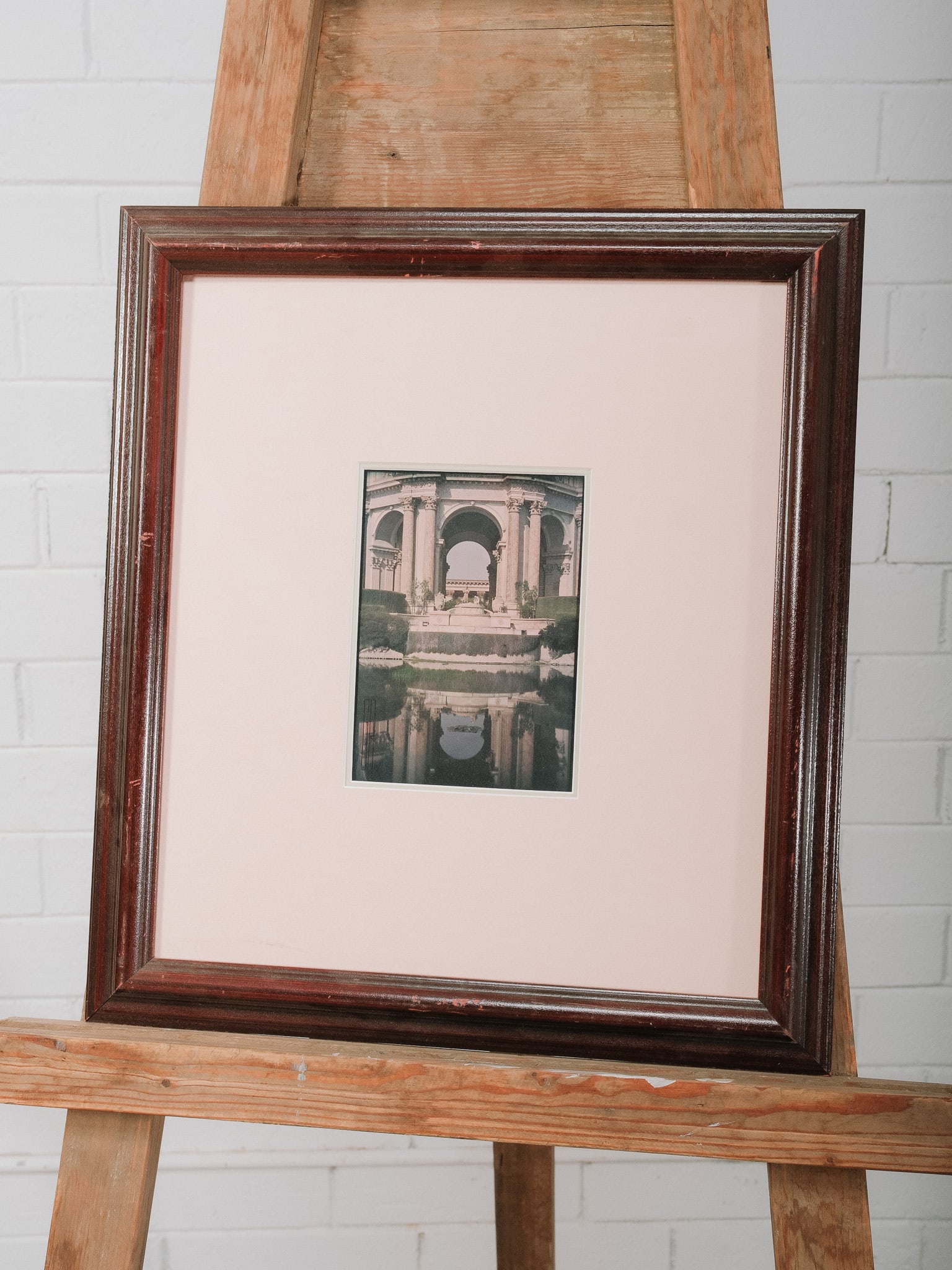 Framed Architectural Print: Framed architectural print depicting a classical arched colonnade reflected in a tranquil pool. Presented beneath a wide cream mat in a dark wood frame, the composition offers a timeless, understated 