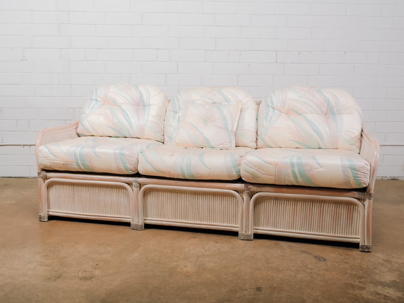 Three-Seat Coastal Rattan Sofa: Three-seat rattan sofa featuring a whitewashed finish with decorative wrapped accents and loose pastel upholstered cushions. Its relaxed coastal styling makes it well suited for a sunroom, beach