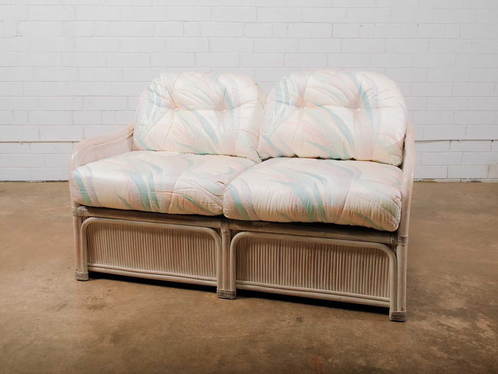 Two-Seat Coastal Rattan Loveseat: Two-seat rattan loveseat featuring a whitewashed finish with decorative wrapped accents and loose pastel upholstered cushions. A comfortable seating option for a sunroom, covered porch, or