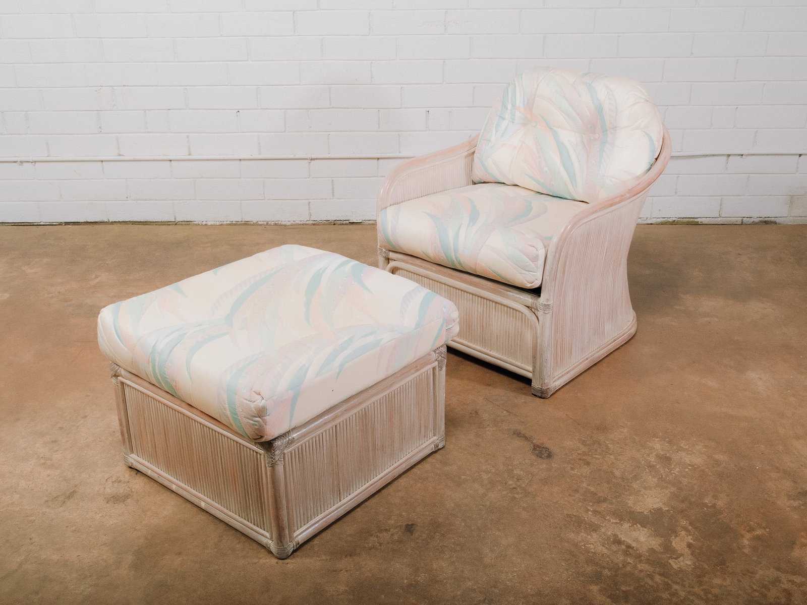 Cream Reed Chair and Ottoman: Whitewashed rattan lounge chair with matching ottoman, each featuring loose pastel upholstered cushions and decorative wrapped accents. A comfortable seating set perfect for a sunroom, screened