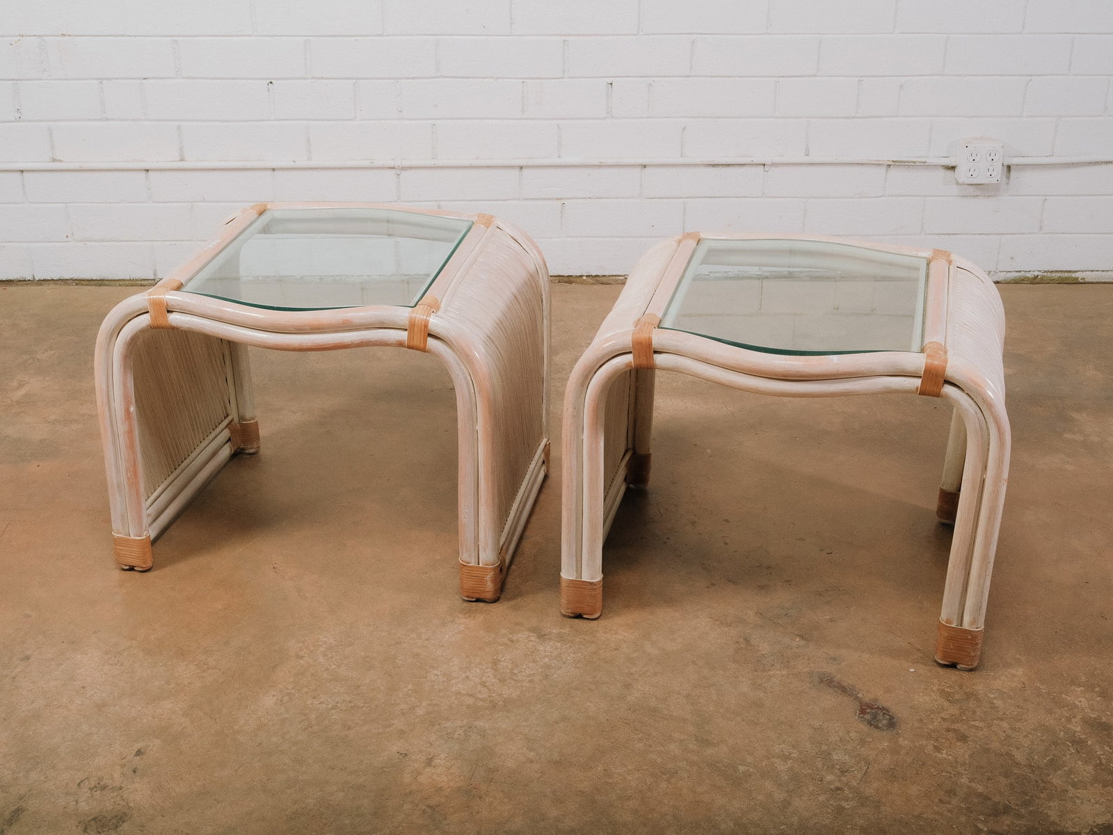 Pair of Coastal Rattan Glass Side Tables: Pair of bent rattan side tables with inset glass tops, light washed finish, and wrapped rattan accents. Coastal-inspired design.Approximate Dimensions: 20.5"h x 25"w x 22"d