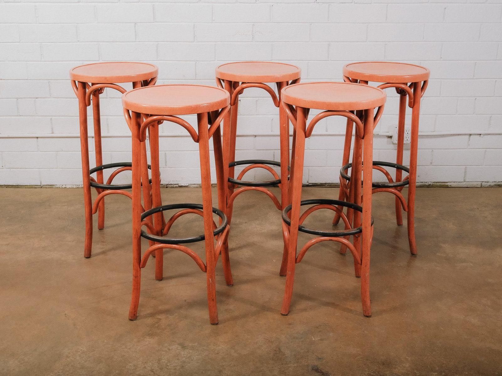 Set of 5 Bentwood Bar Stools: Set of five bentwood bar stools featuring round seats, classic curved supports, and circular metal footrests. Finished in a coral-painted finish, these stools bring a playful pop of color to kitchen i