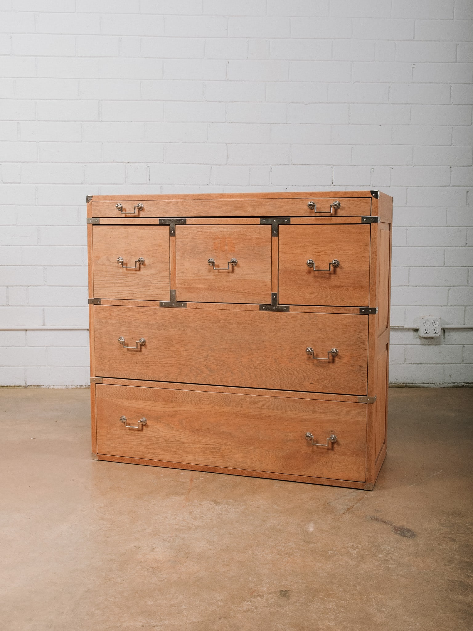 Campaign Style Oak Chest: Campaign-style oak chest featuring seven drawers with brass corner brackets, recessed hardware, and clean architectural lines. The functional design offers generous storage while blending classic camp