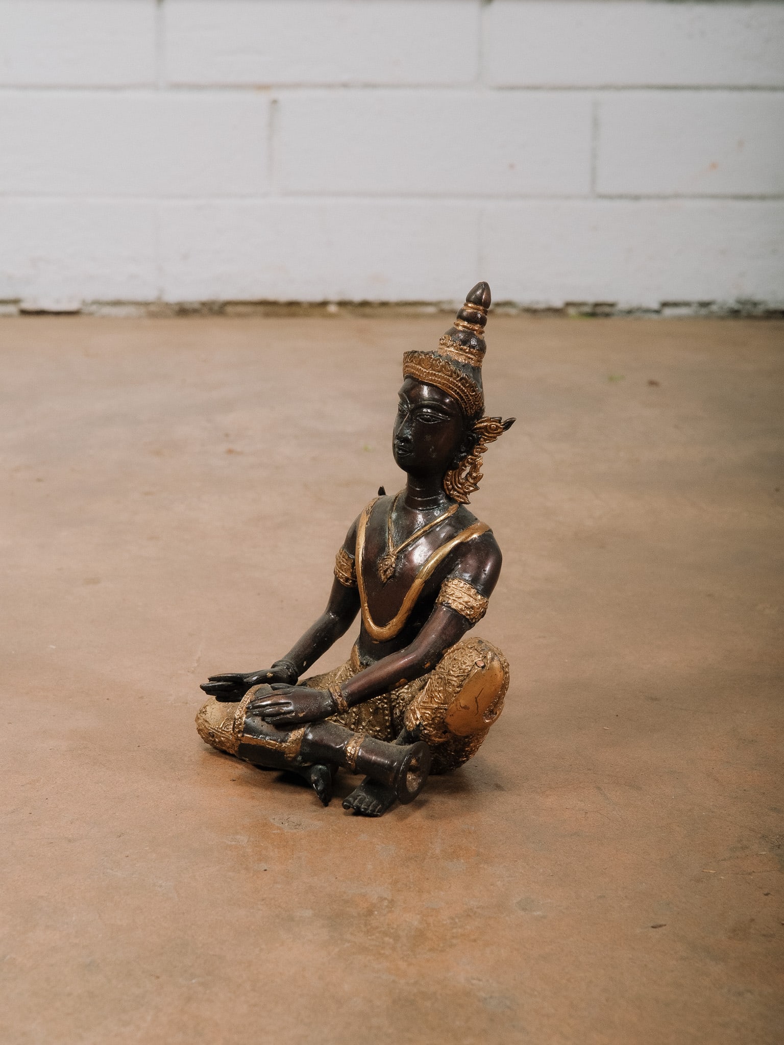 Thai Seated Figure: Thai-style metal figure seated in a traditional pose with gilt accents and decorative headdress. A decorative Southeast Asian sculpture.Approximate Dimensions: 7.5"h x 6"w x 4"d