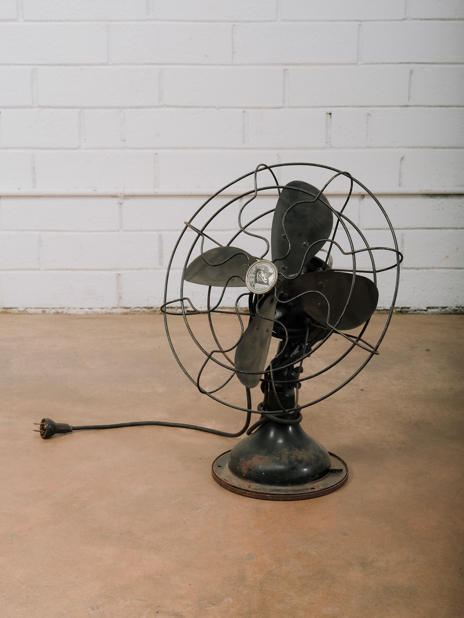 Vintage R&M Electric Desk Fan: Vintage R&M Electric desk fan featuring a black painted metal finish, four-blade propeller, and original wire safety cage. The fan retains its classic industrial styling with an adjustable head and