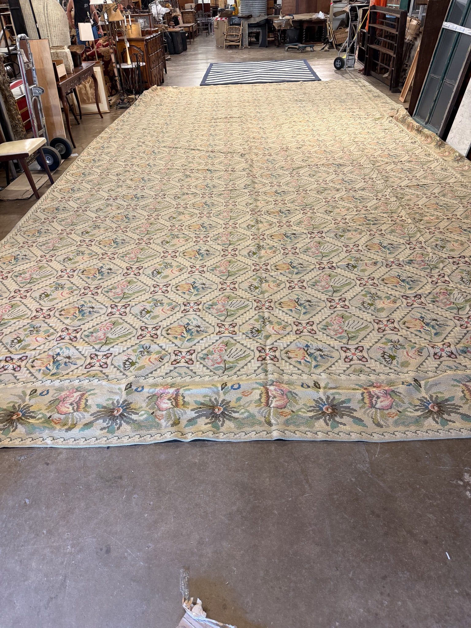 Oversized Needlepoint Area Rug: Oversized needlepoint area rug featuring an intricate floral and geometric design in soft shades of blue, ivory, gold, and muted rose with a coordinating decorative border. Its generous scale makes it