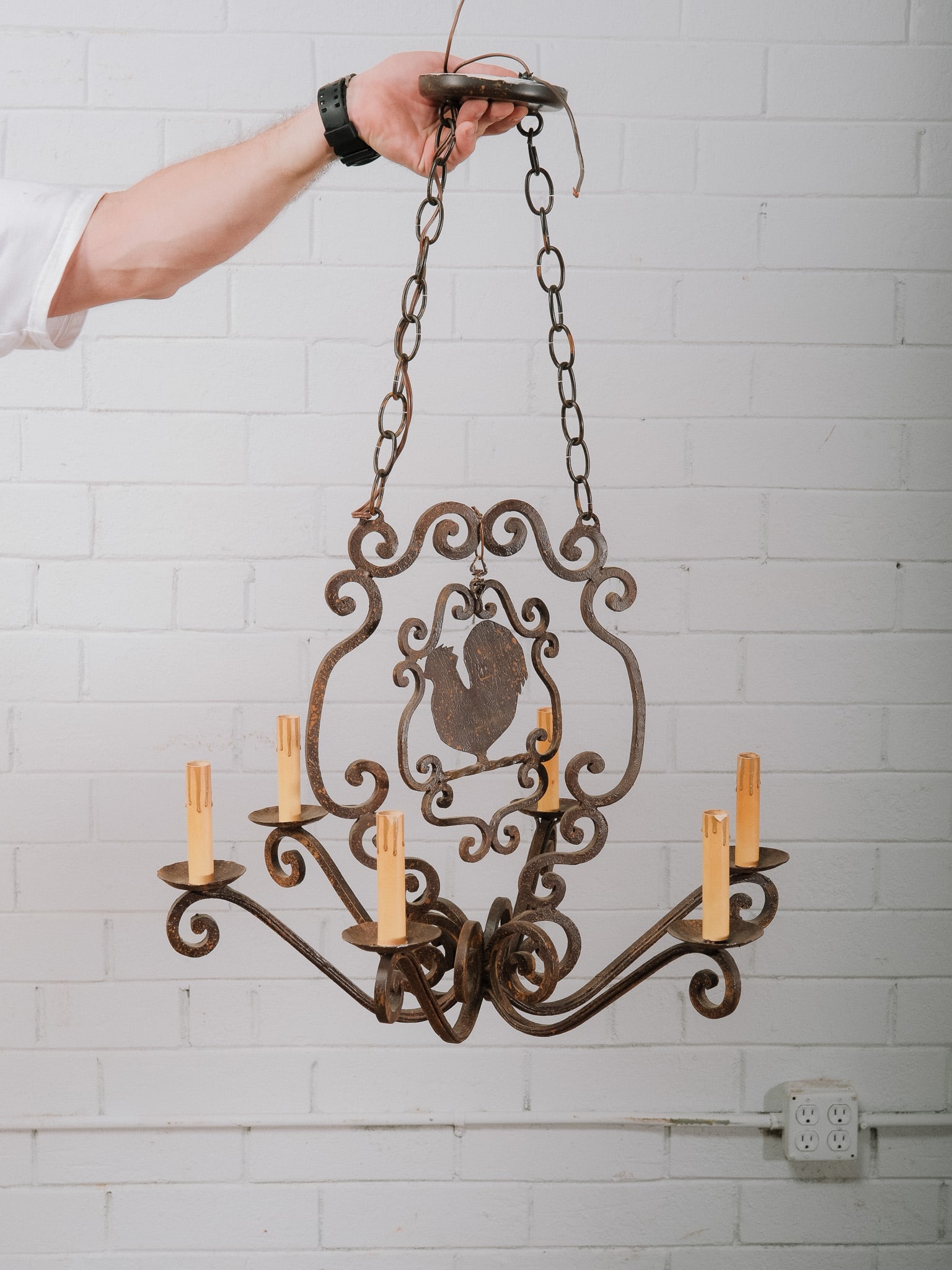 Wrought Iron Six-Light Chandelier with Rooster Motif: Decorative wrought iron six-light chandelier featuring scrolling arms, a central rooster motif, and an antiqued finish. The rustic design is well suited for farmhouse, Tuscan, or French country