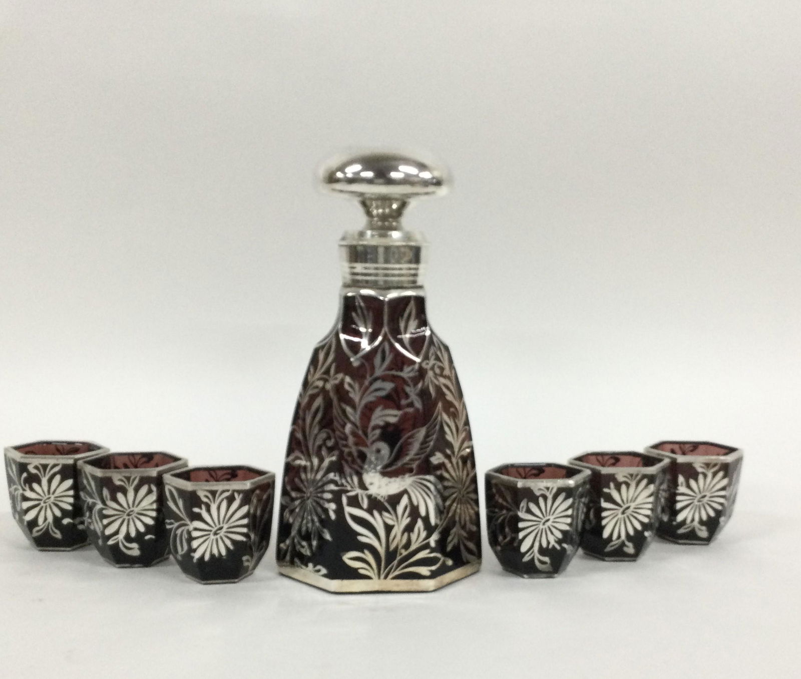 Deep Red Glass and Sterling Silver Overlay Decanter Set: Deep Red Glass and Sterling Silver Overlay Decanter Set. Measuring approximately (decanter) 8.25 tall x 4.25 wide x 2.5 deep, (cups) 2.25 tall x 2.25 wide x 1.5 deep. Weighing approx. 2.8 lbs. For Shi
