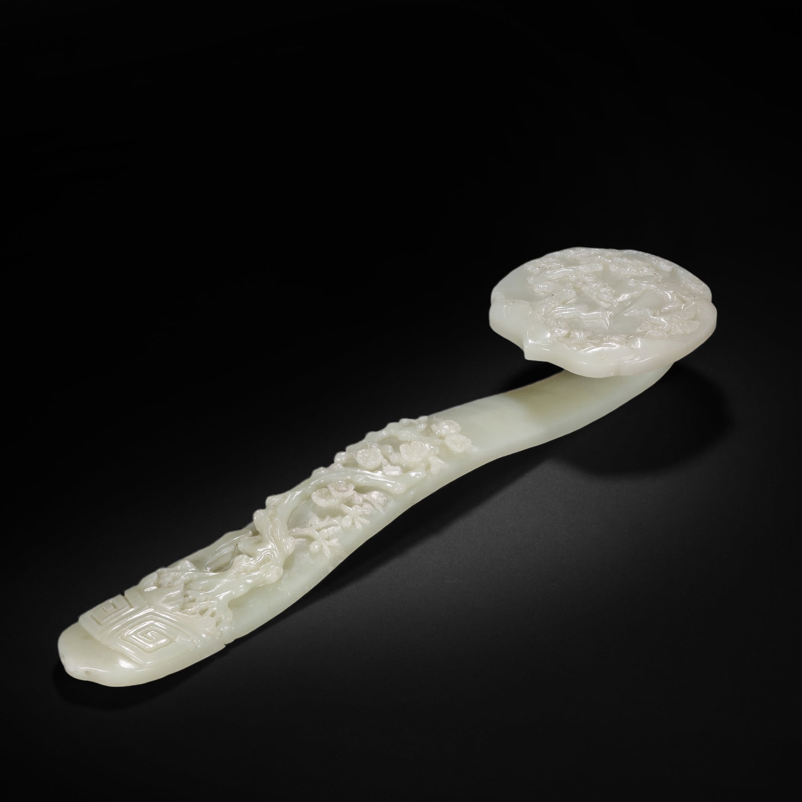 QING DYNASTY HETIAN WHITE JADE CARVED WITH PINE AND PLUM PATTERNS RUYI: H:28.5cm(11.22in) W:7.8cm(3.07in) Weight:390g(0.86lb)This Ruyi is carved from a single piece of Hetian white jade, with a warm and fine texture, as white as curd. The Ruyi head is carved with landscap