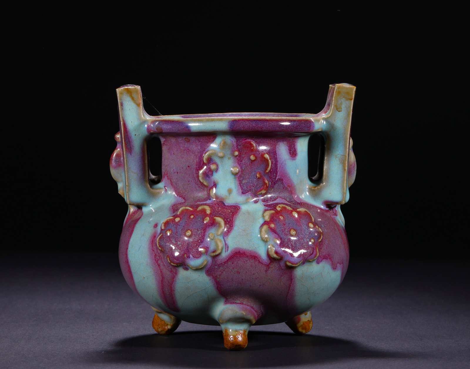 QING DYNASTY JUN KILN SKY BLUE GLAZED PURPLE SPOTTED THREE-LEGGED FURNACE: H:13cm(5.12in) W:12cm(4.72in)This censer is a classic display ritual vessel of Jun Kiln, featuring a straight mouth, bulging belly, double vertical ears on the rim, three-dimensional relief flower pat