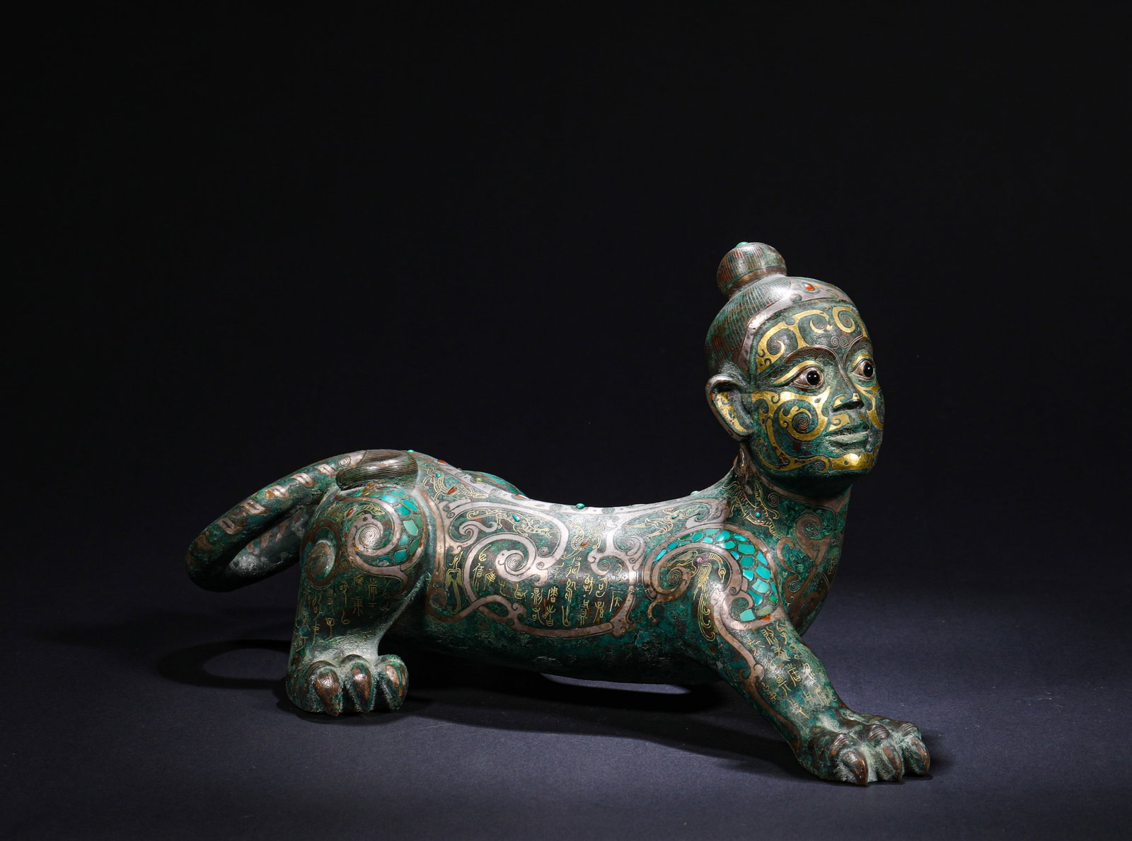 SHANG DYNASTY INLAID GOLD AND SILVER WITH GEMSTONES, HUMAN FACE AND ANIMAL BODY BRONZE TOWN: H:16cmW:29cmWeight:2620g This is a bronze paperweight with a human-faced beast body, inlaid with gemstones and decorated with gold and silver inlay. Featuring a unique human-faced beast shape, it is e
