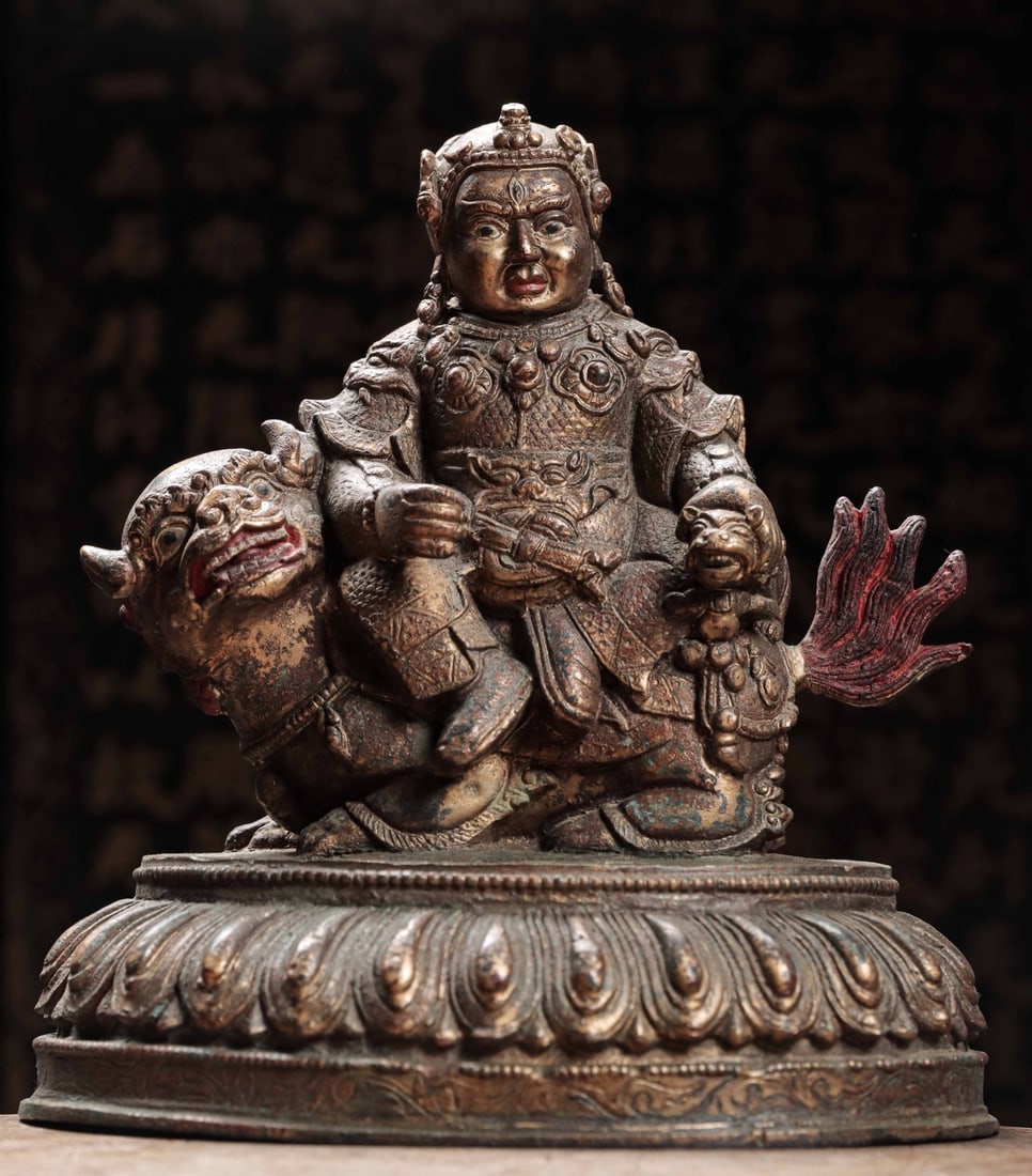 A GILDED BRONZE STATUE OF THE KING OF TREASURES FROM THE QING DYNASTY: Weight:5000g(11.03lb)H:13cm(5.12in)W:20.6cm(8.11in)T:14.5cm(5.71in)This Vaishravana statue sits solemnly on an auspicious lion mount, with wrathful majestic facial features, wearing a divine crown and