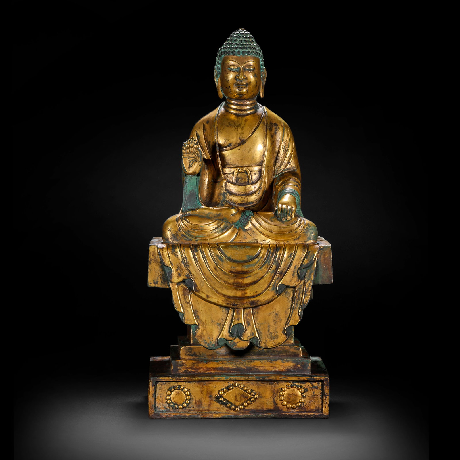 A GILDED BRONZE SEATED STATUE OF SAKYAMUNI BUDDHA FROM THE NORTHERN WEI DYNASTY: H:38cm(14.96in) W:18cm(7.09in) Weight:10670g(23.52lb)This statue is cast in bronze and gilded. Sakyamuni Buddha sits in the lotus position on a square pedestal, with a high ushnisha and a solemn appea