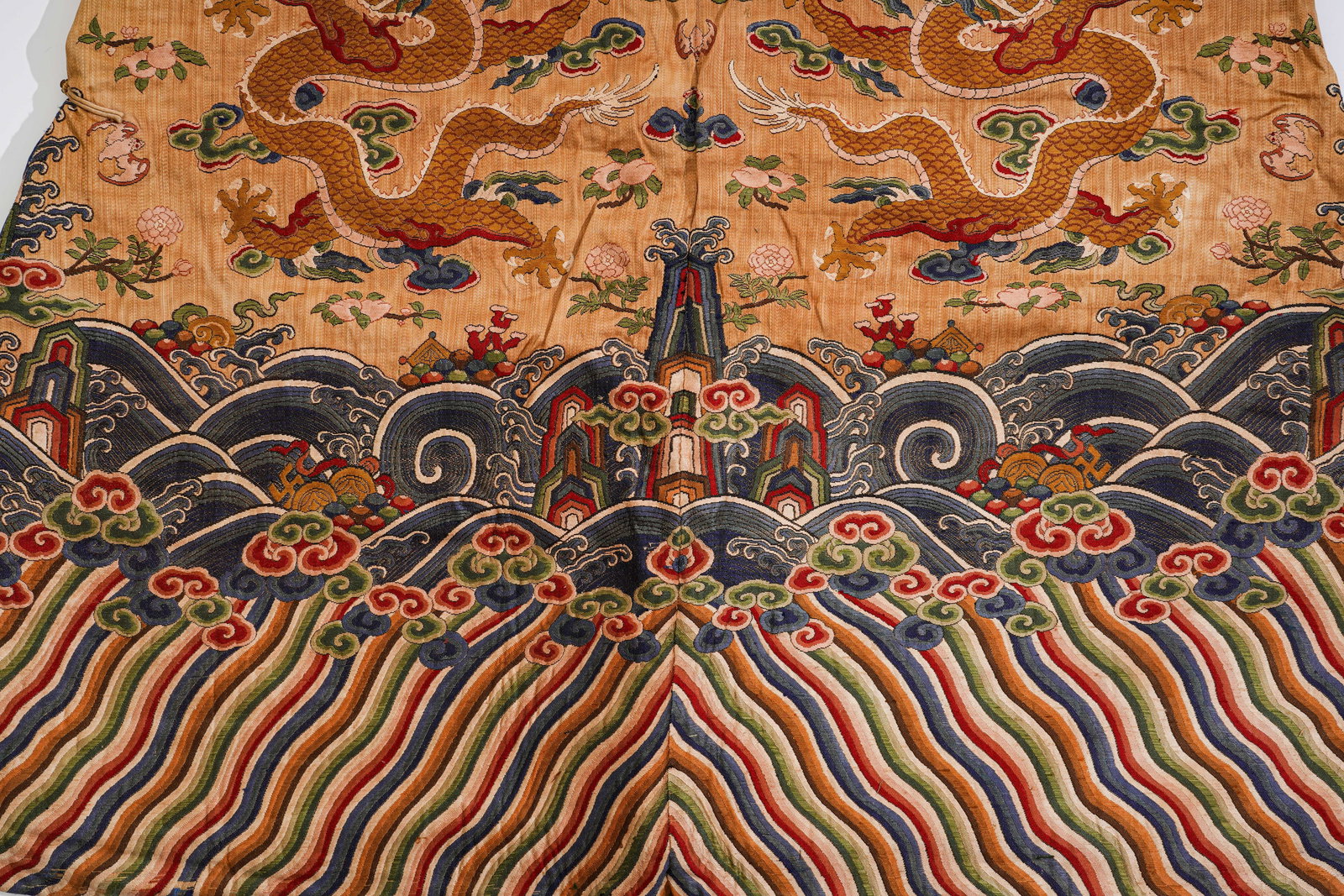 THE QING DYNASTY'S APRICOT-YELLOW KESI ROBE WITH NINE DRAGON PATTERNS: H:136cm(53.54in) W:199cm(78.35in)This dragon robe is a national treasure of Qing Dynasty court attire. With an apricot-yellow kesi base, it adopts the "passing warp and breaking weft" kesi technique t